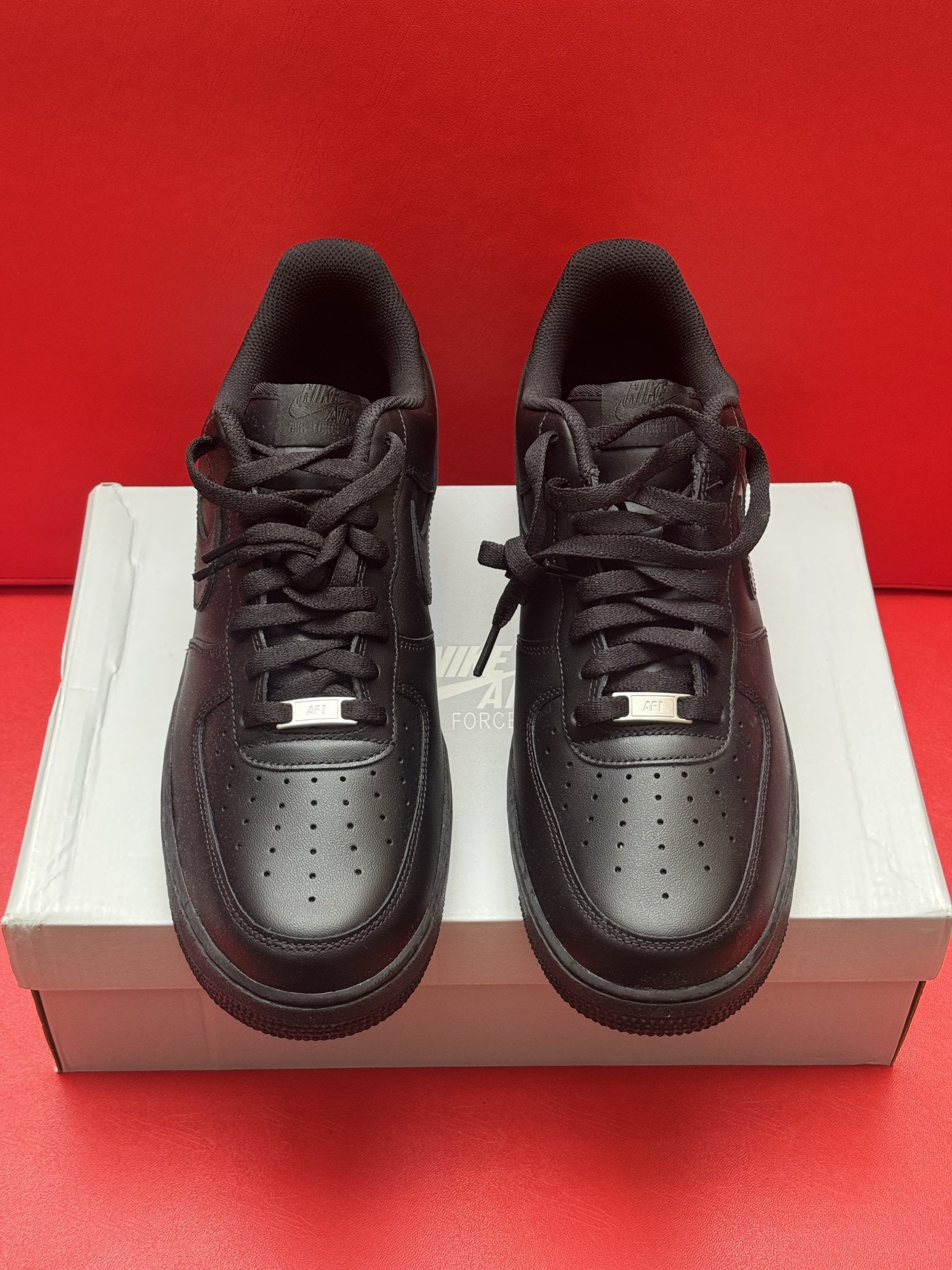 Black Nike Air Force 1 sneakers on a white box, set against a red background.