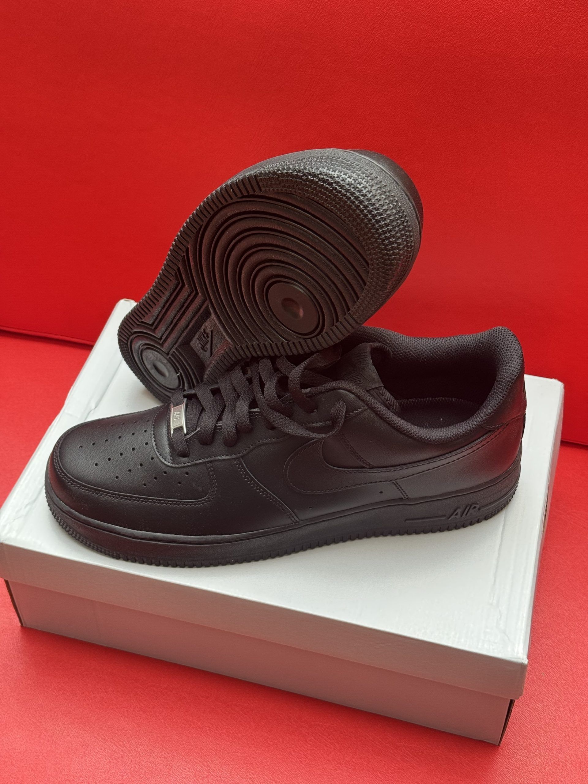 Black Nike Air Force 1 sneakers on a white box, set against a red background.