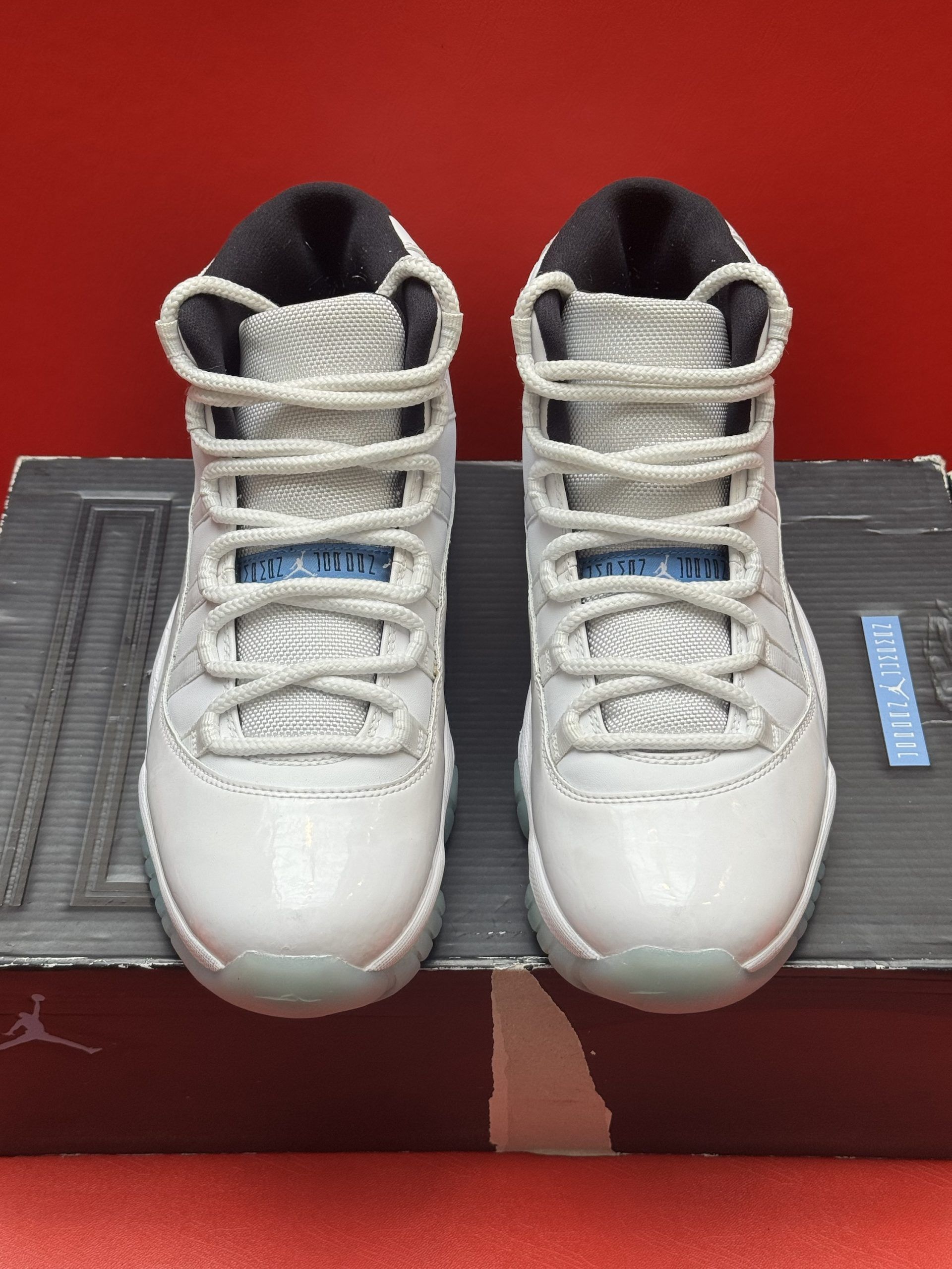 White and blue Air Jordan 11 sneakers on a shoe box with a red background.