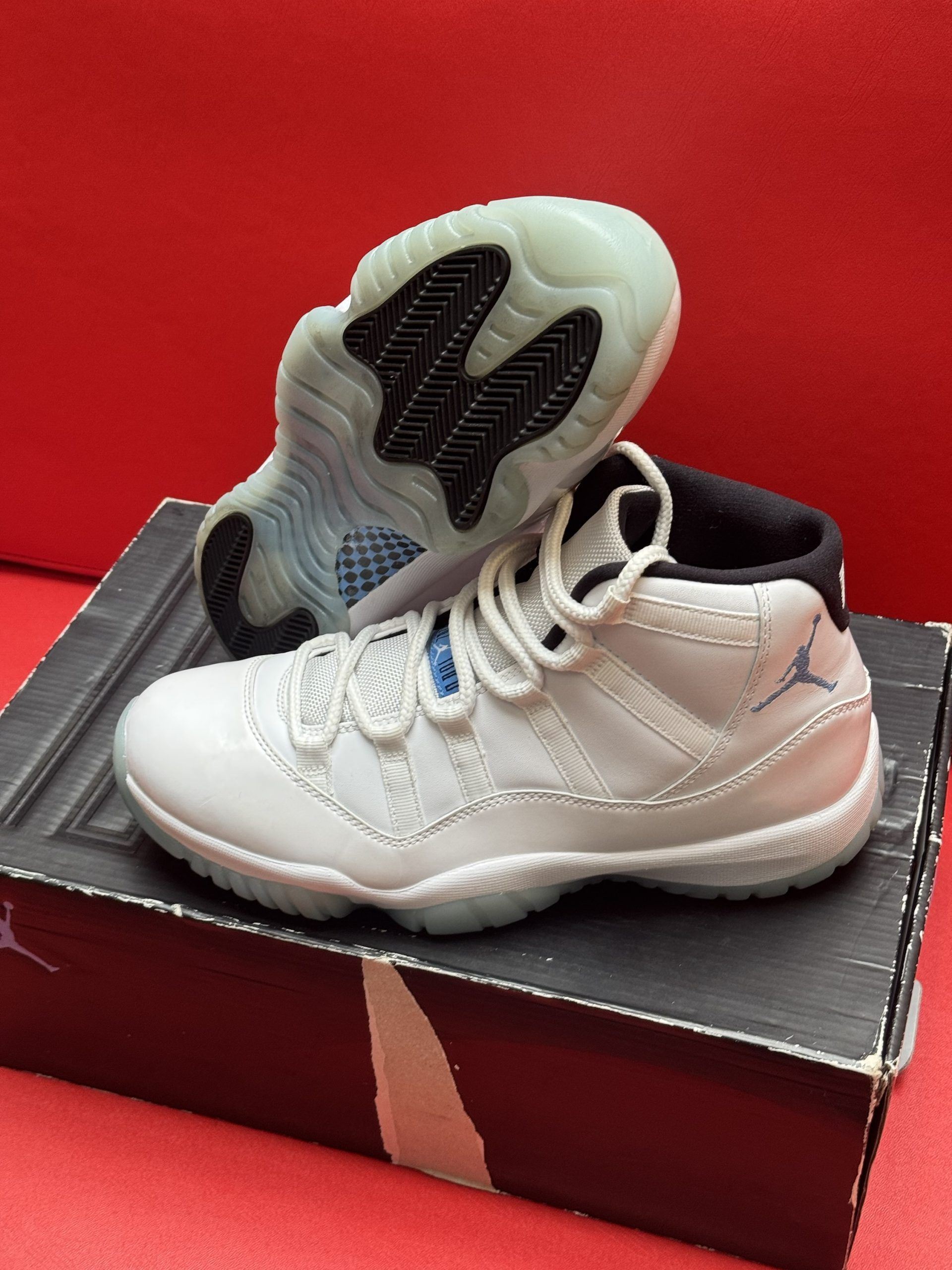 White and blue Air Jordan 11 sneakers on a shoe box with a red background.