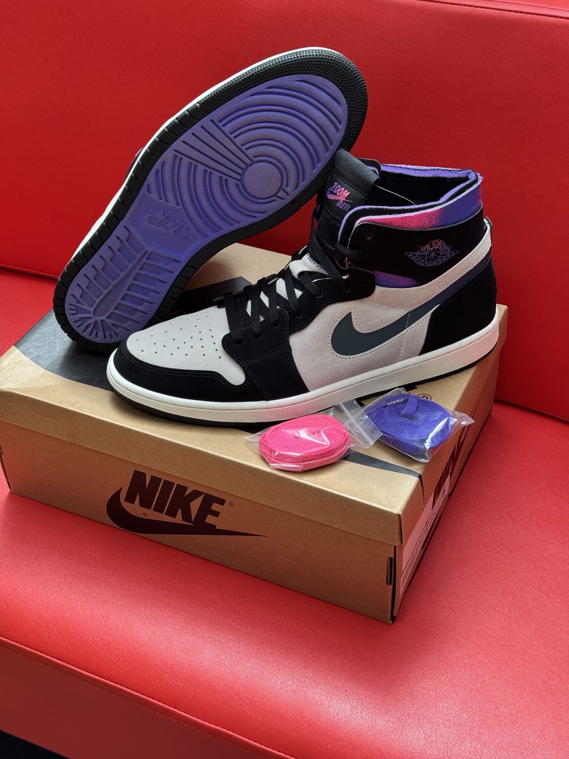Air Jordan 1 sneakers on shoebox, purple sole, with extra laces and pink accessories.