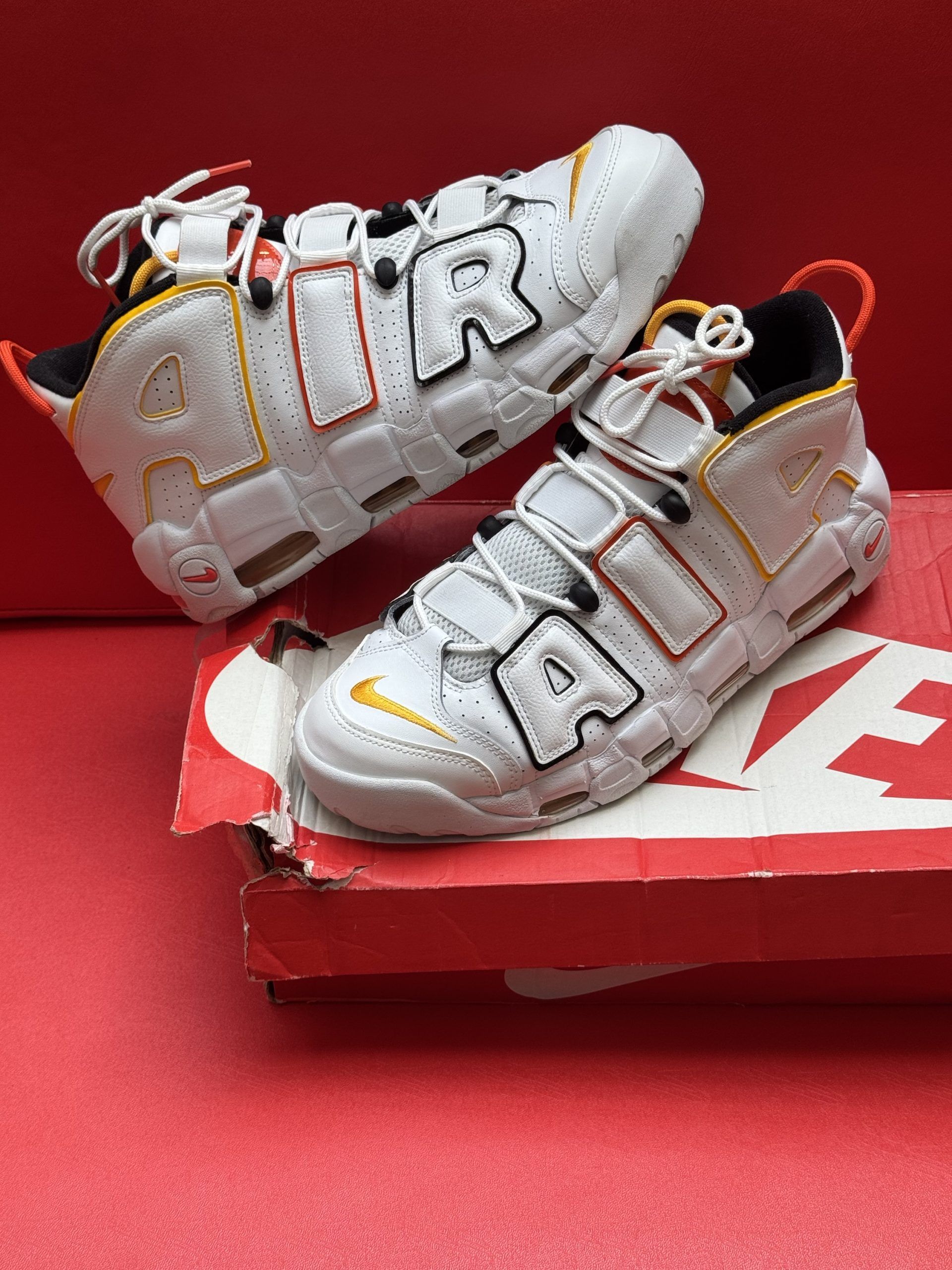 White Nike Air More Uptempo sneakers on a red box with red sole, orange and yellow accents.