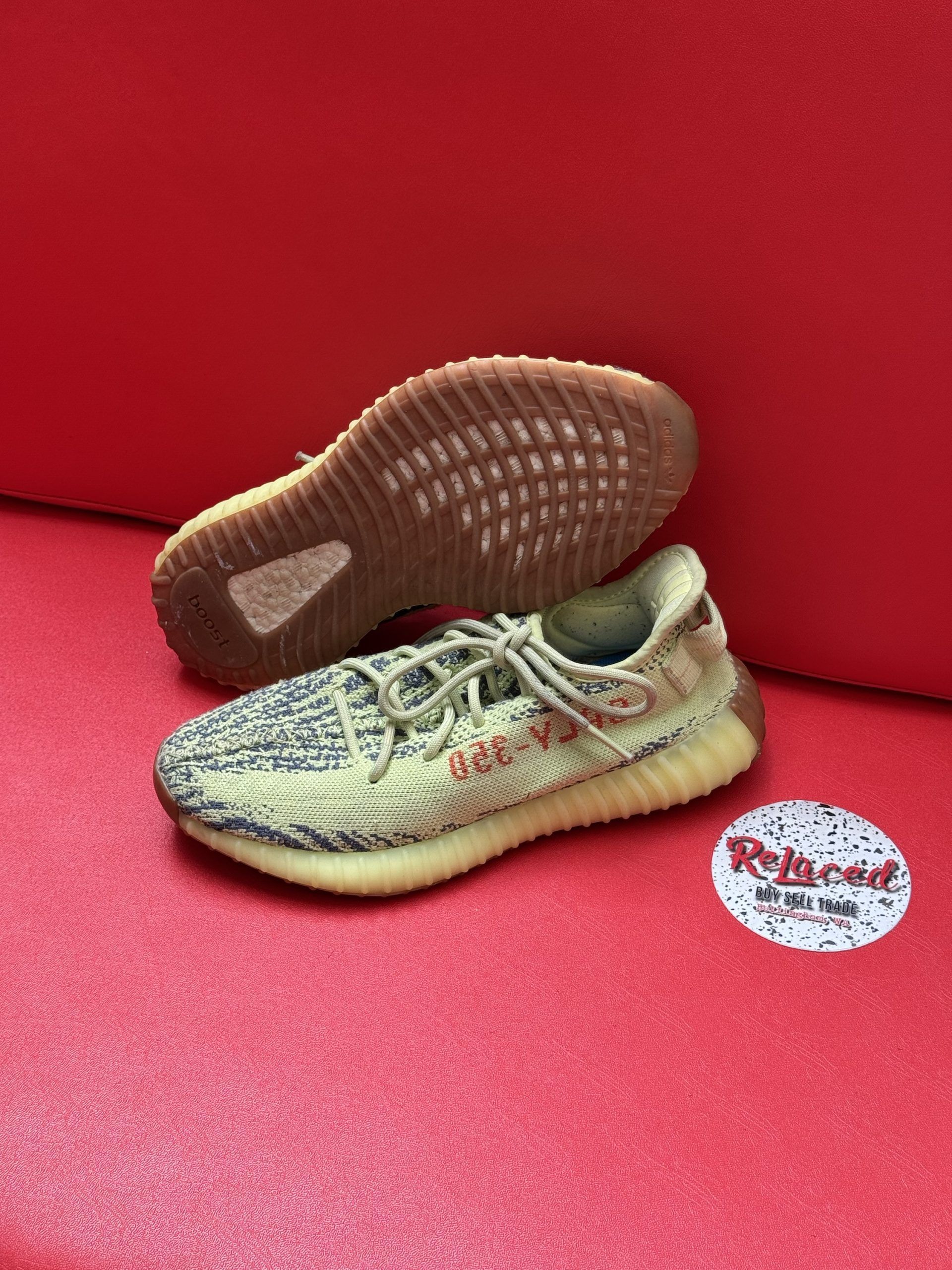 Yeezy Boost 350 V2 sneakers with a tan and green pattern on a red surface; one sole visible.