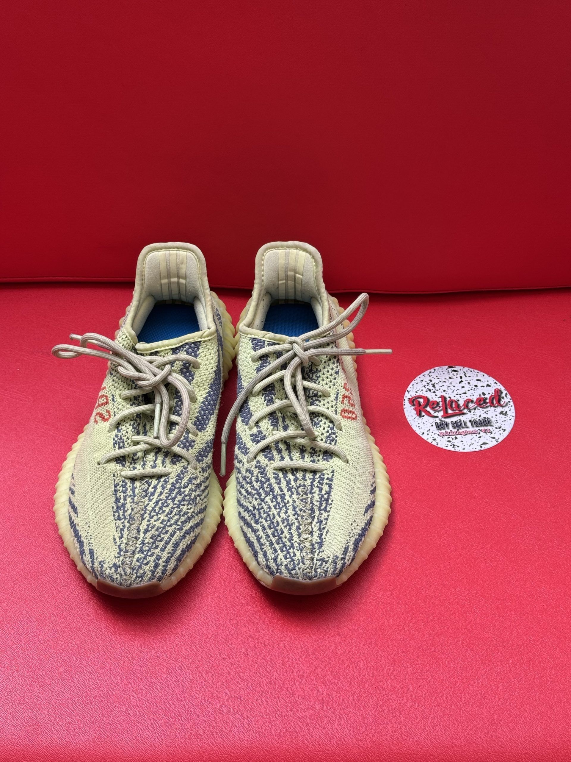 Yeezy Boost 350 V2 sneakers with a tan and green pattern on a red surface; one sole visible.