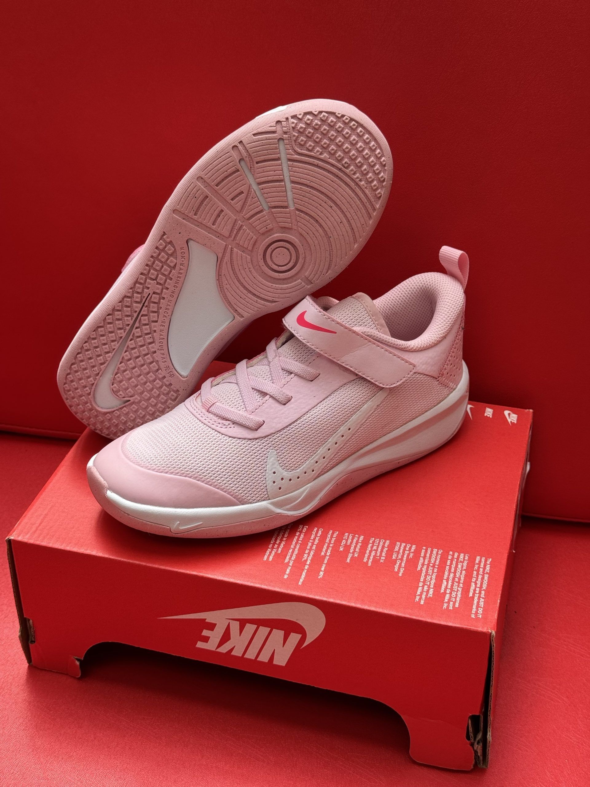 Pink Nike sneakers on a red box; sole visible, red background.