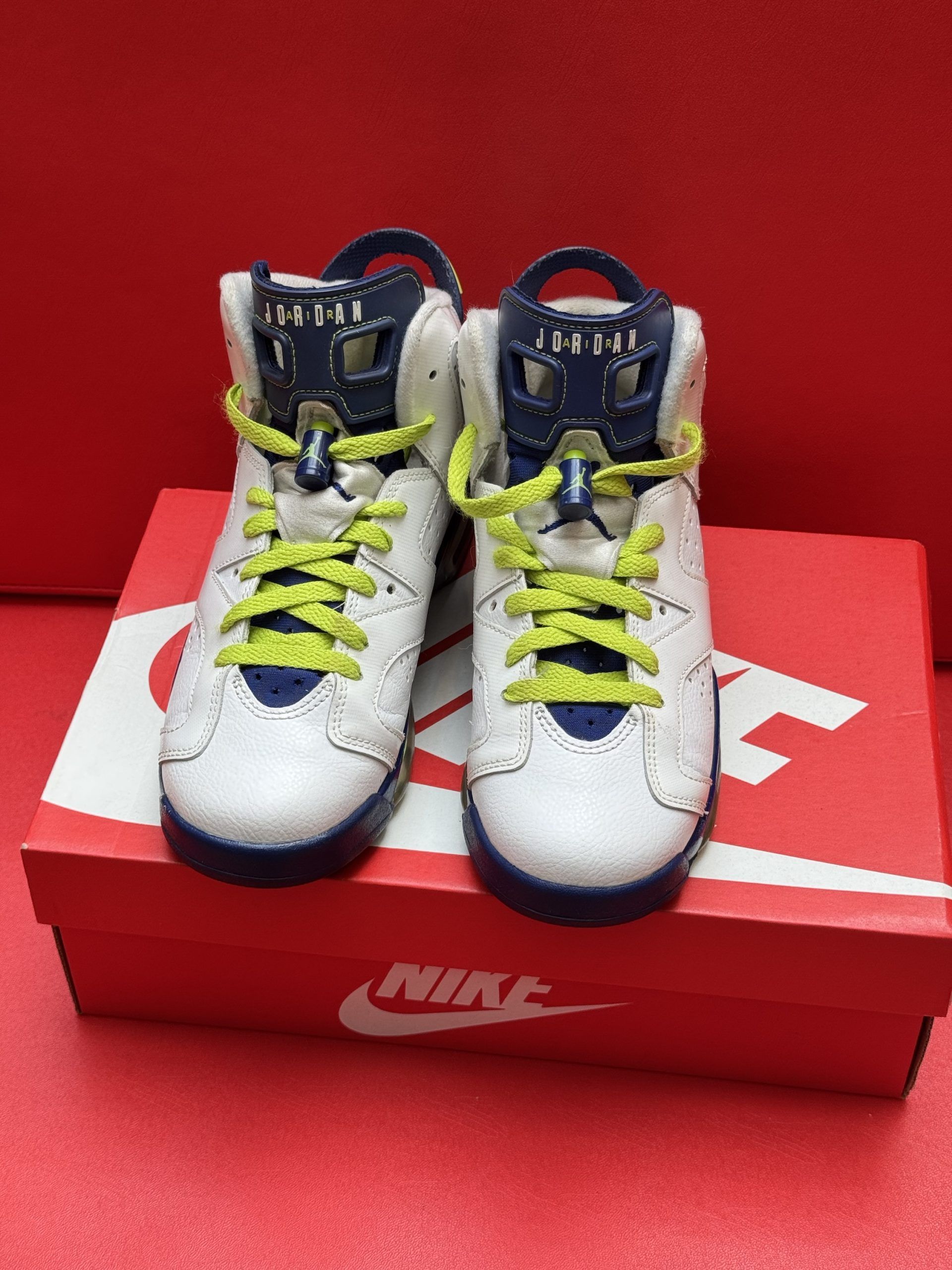 White and blue Air Jordan 6 sneakers with yellow laces sit on a red Nike box.