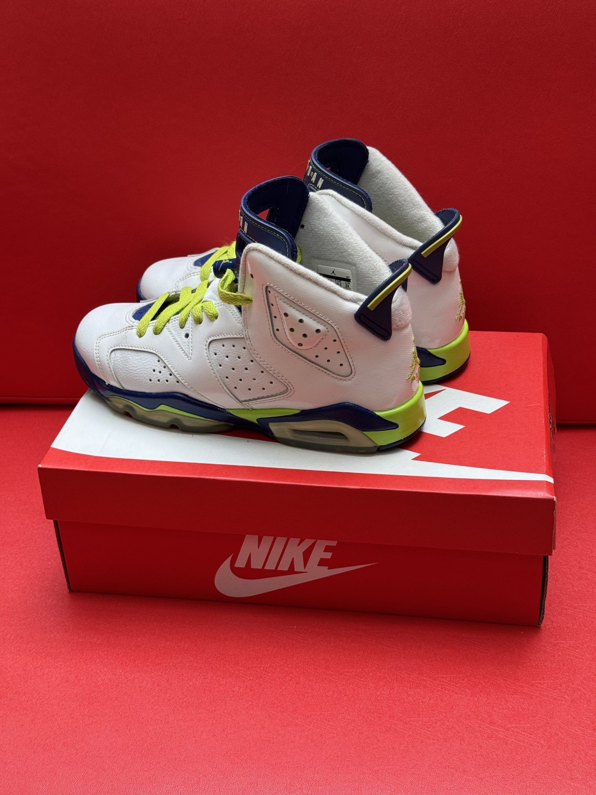 White and blue Air Jordan 6 sneakers with yellow laces sit on a red Nike box.