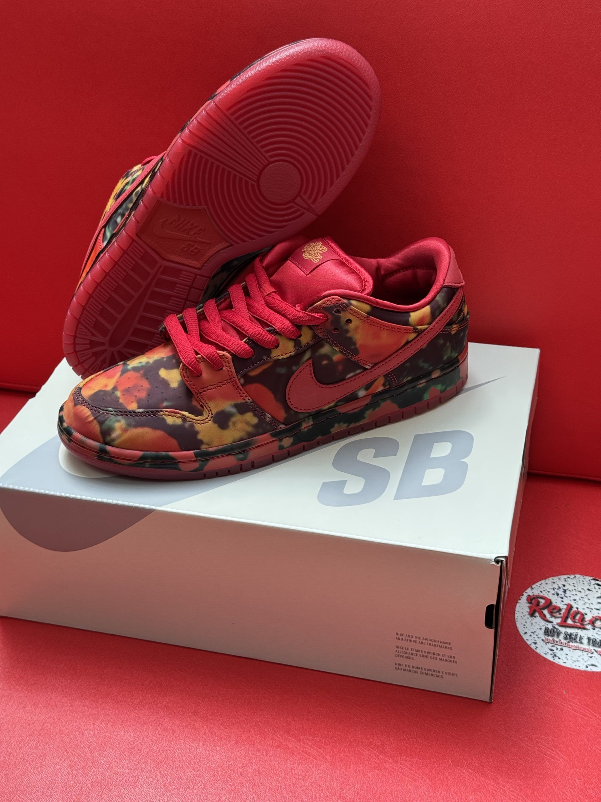 Red and floral patterned Nike SB Dunk Low sneakers on a white box with a red background.