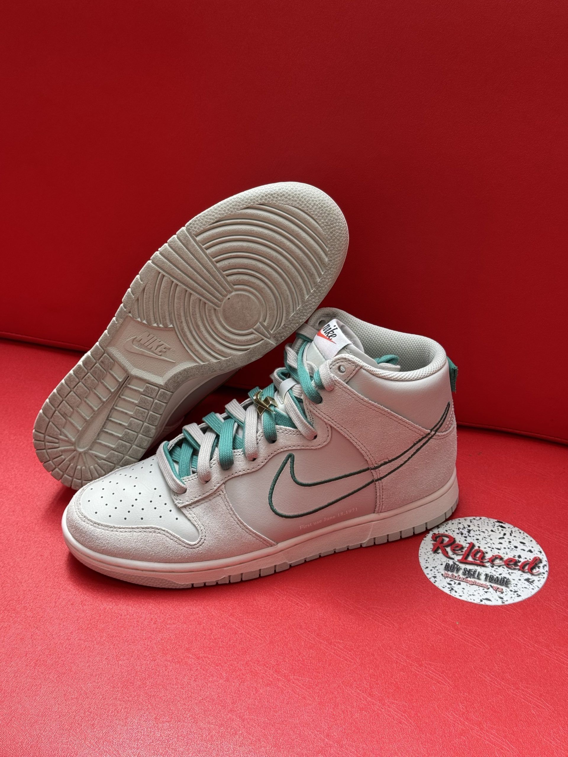 White and teal Nike Dunk High sneakers on a red surface, sole facing up.
