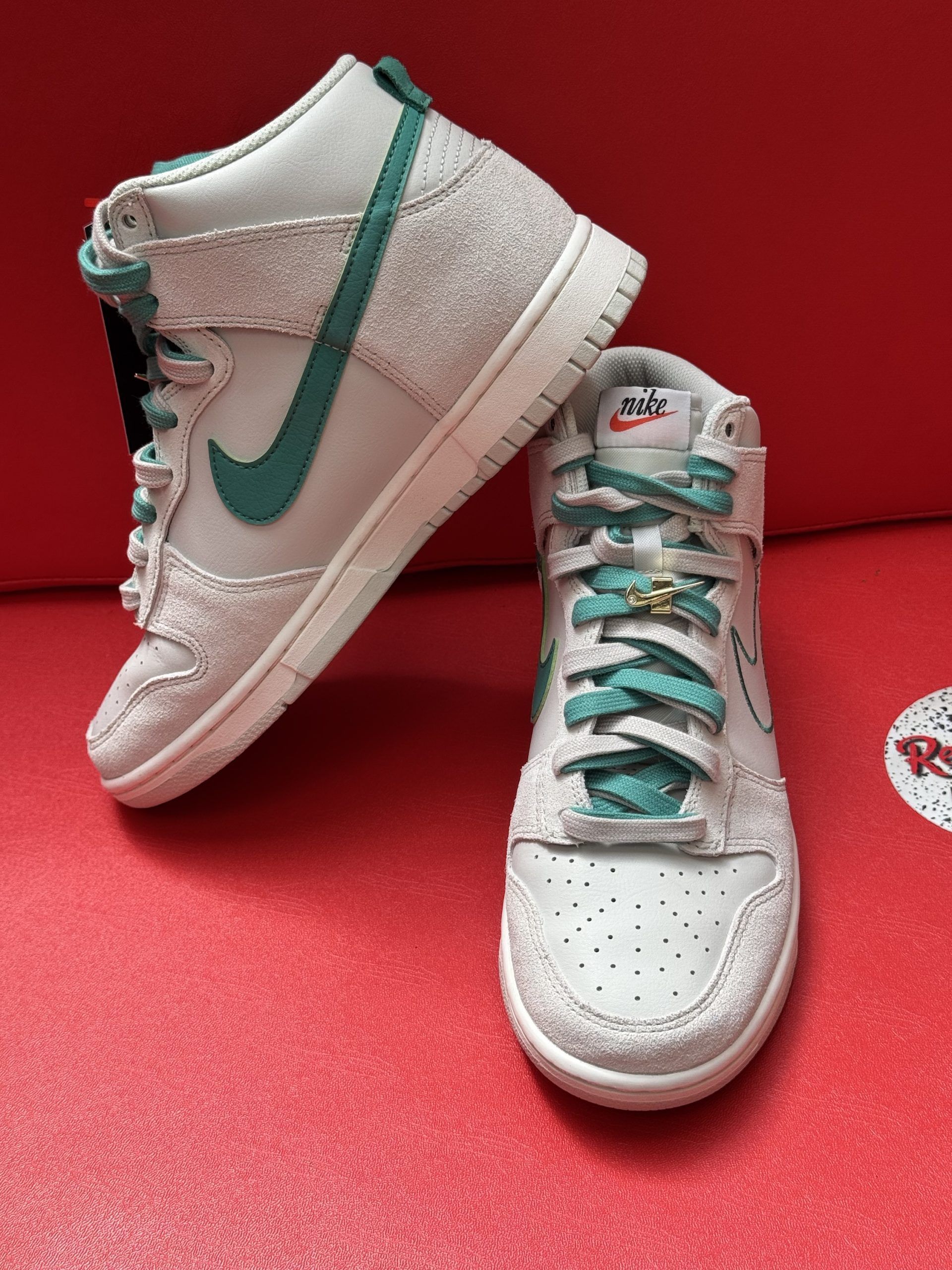 White and teal Nike Dunk High sneakers on a red surface, sole facing up.