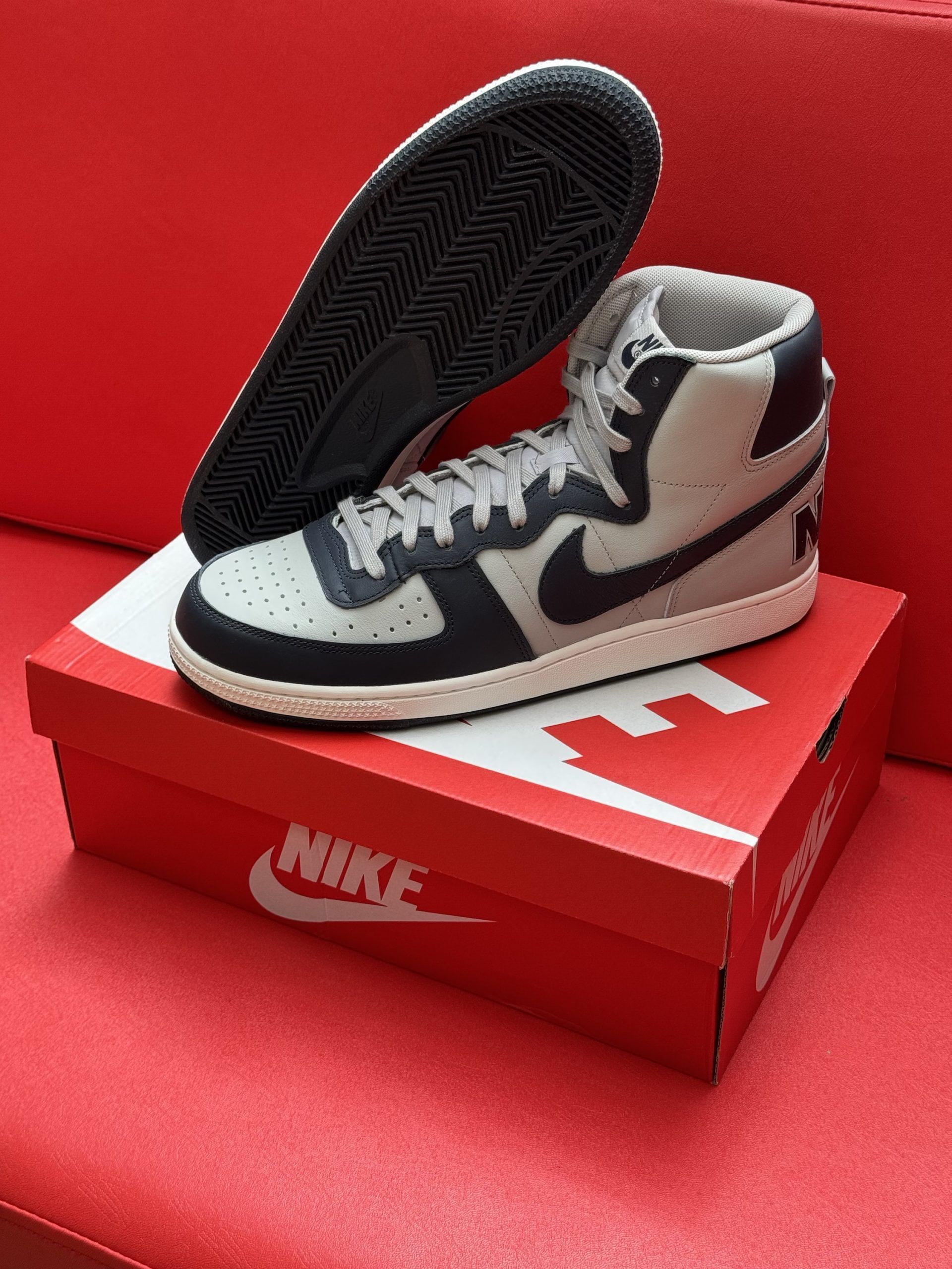 Nike high-top sneakers with a gray and black design, placed on a red Nike shoe box. The sole is visible.
