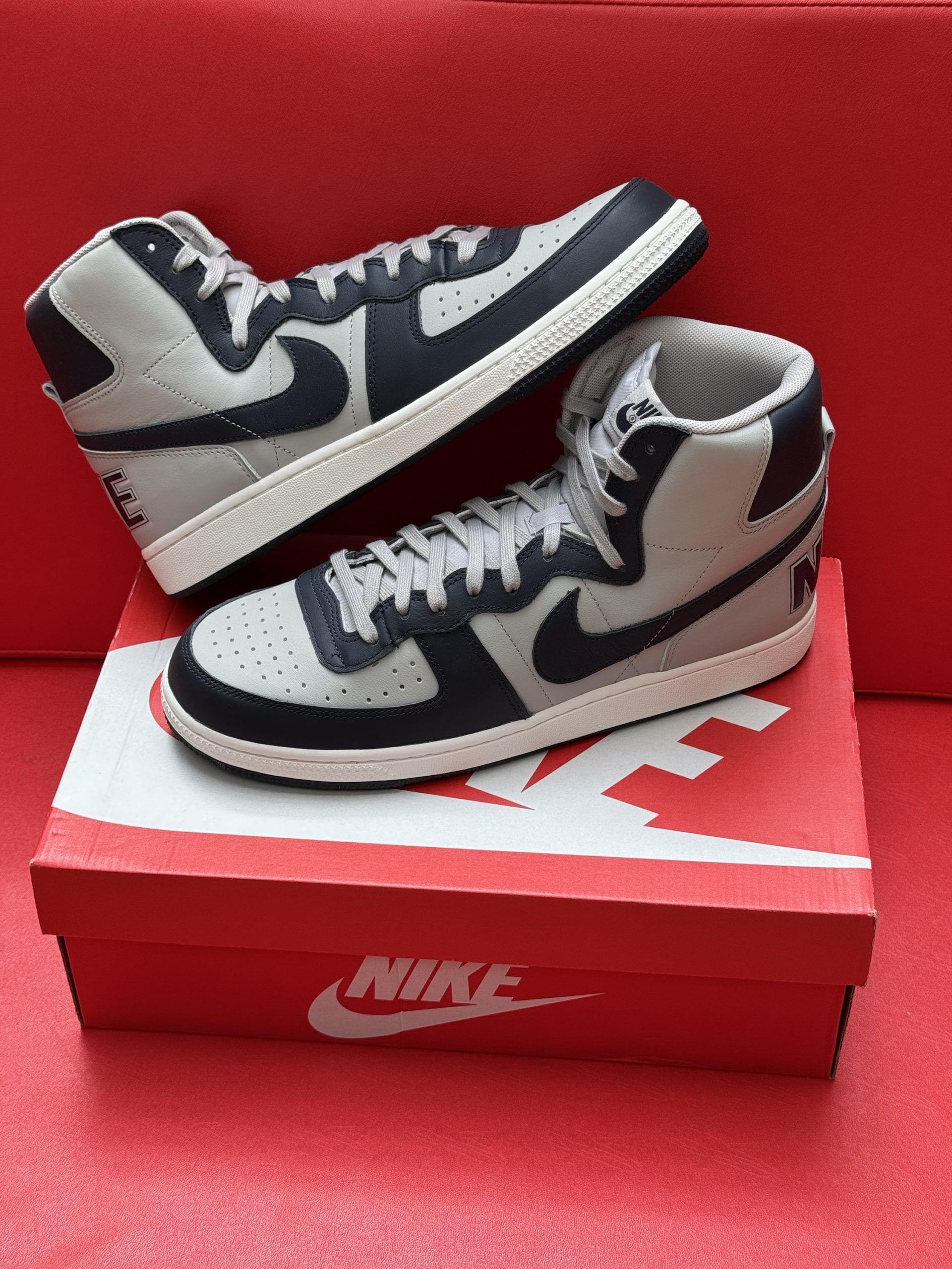 Nike high-top sneakers with a gray and black design, placed on a red Nike shoe box. The sole is visible.