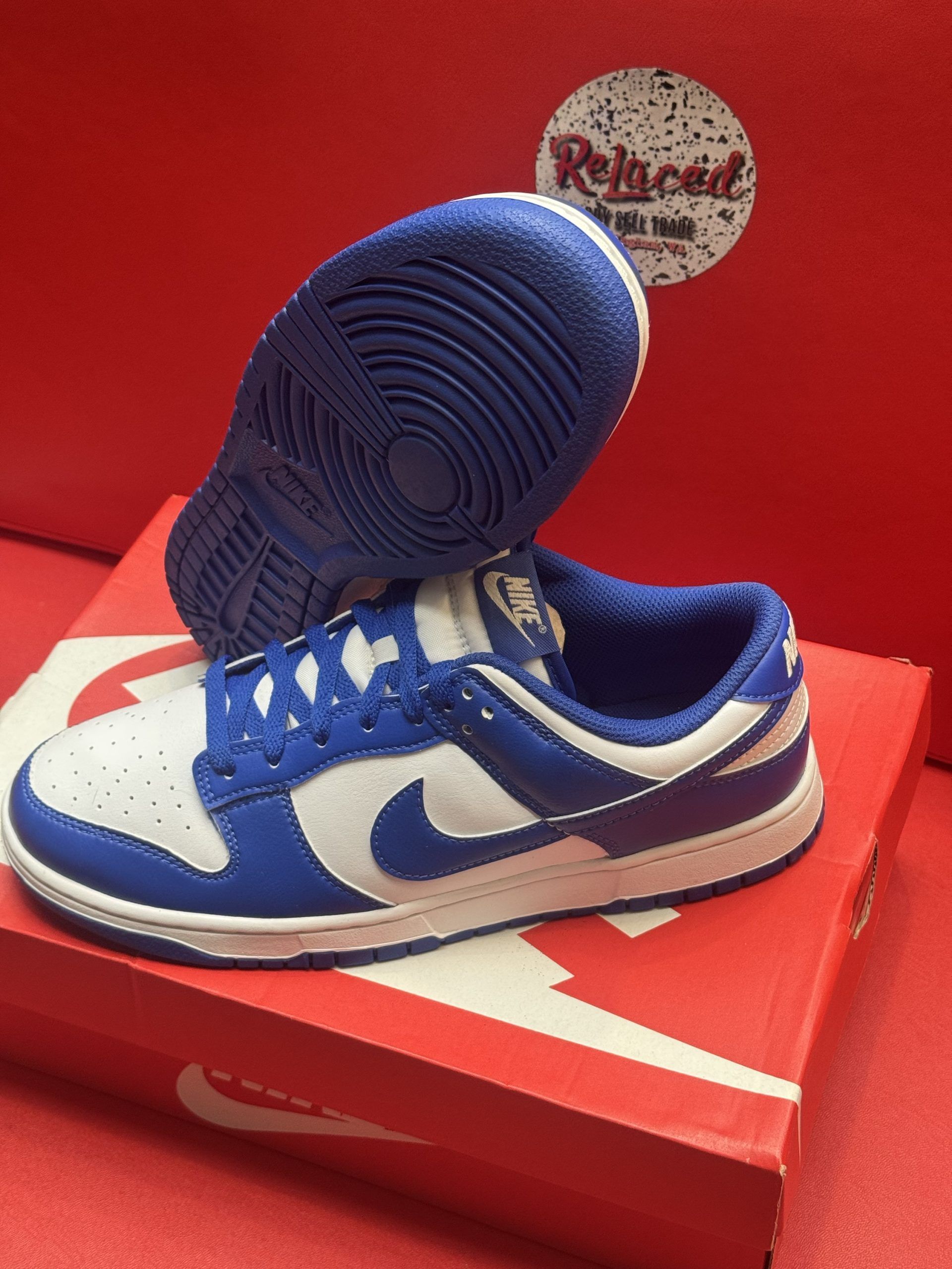Blue and white Nike Dunk Low sneakers on a red Nike shoebox, with a blue sole visible.