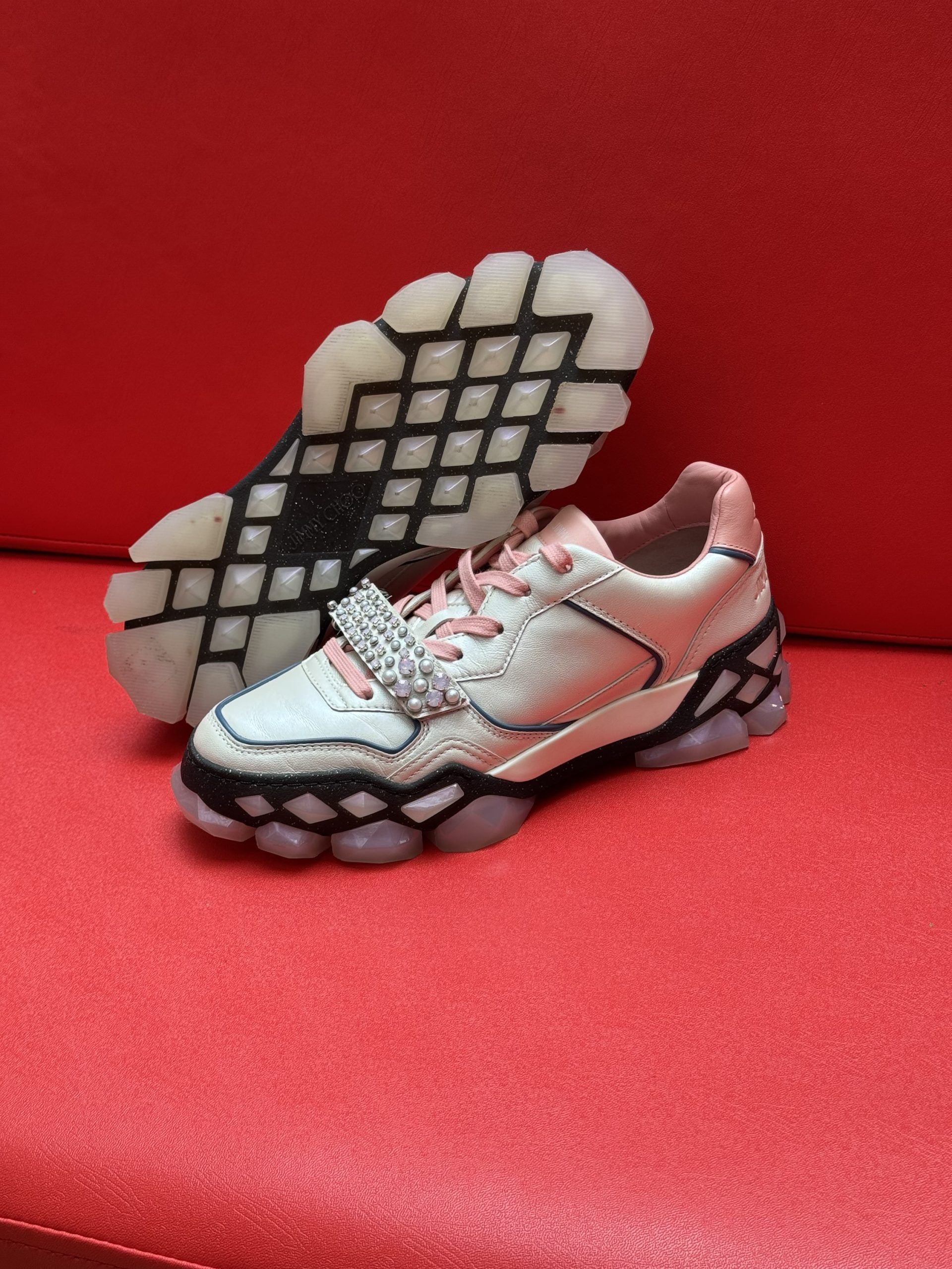 White and pink sneakers with a textured sole, resting on a red surface.