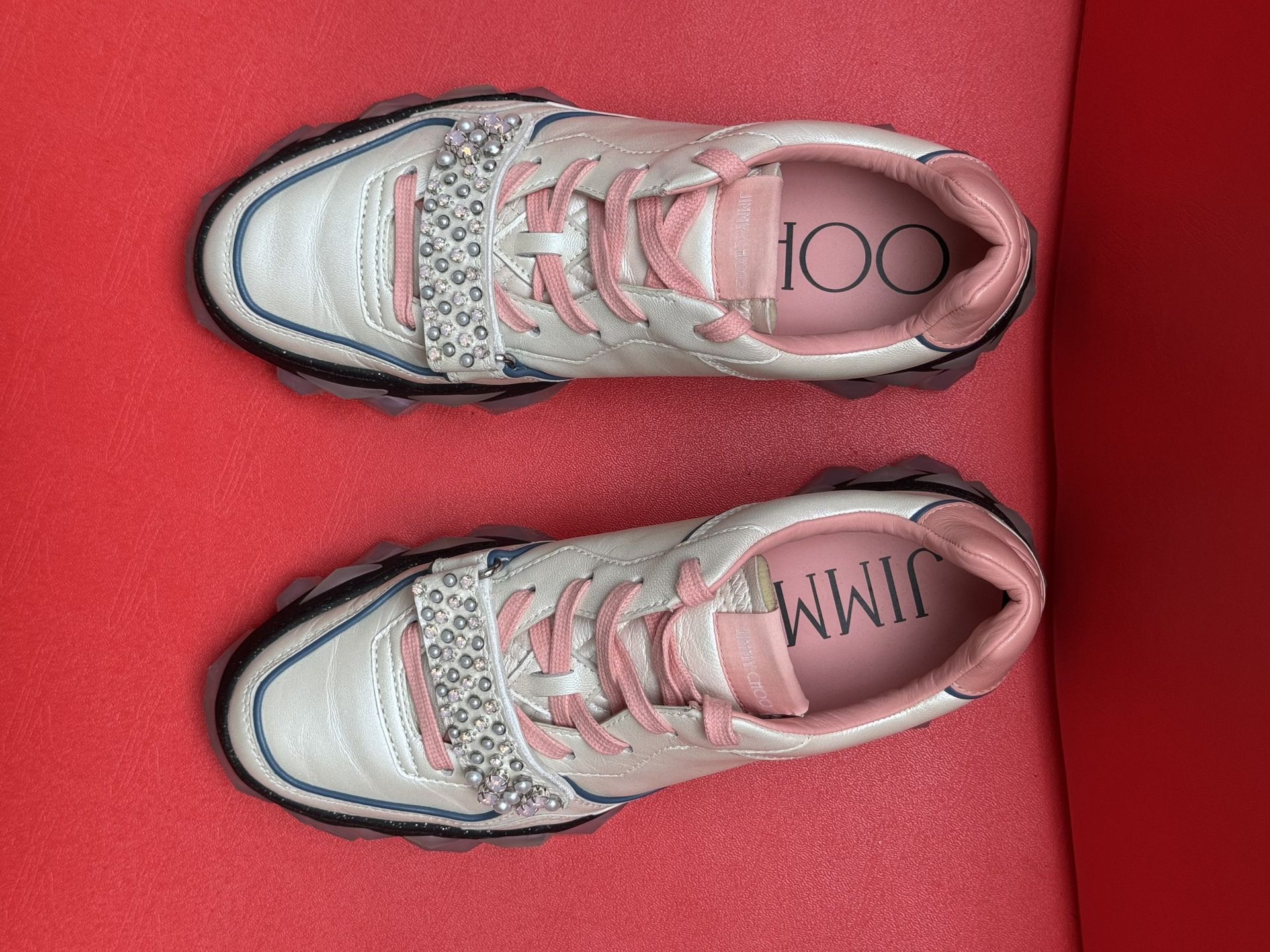 White and pink sneakers with a textured sole, resting on a red surface.