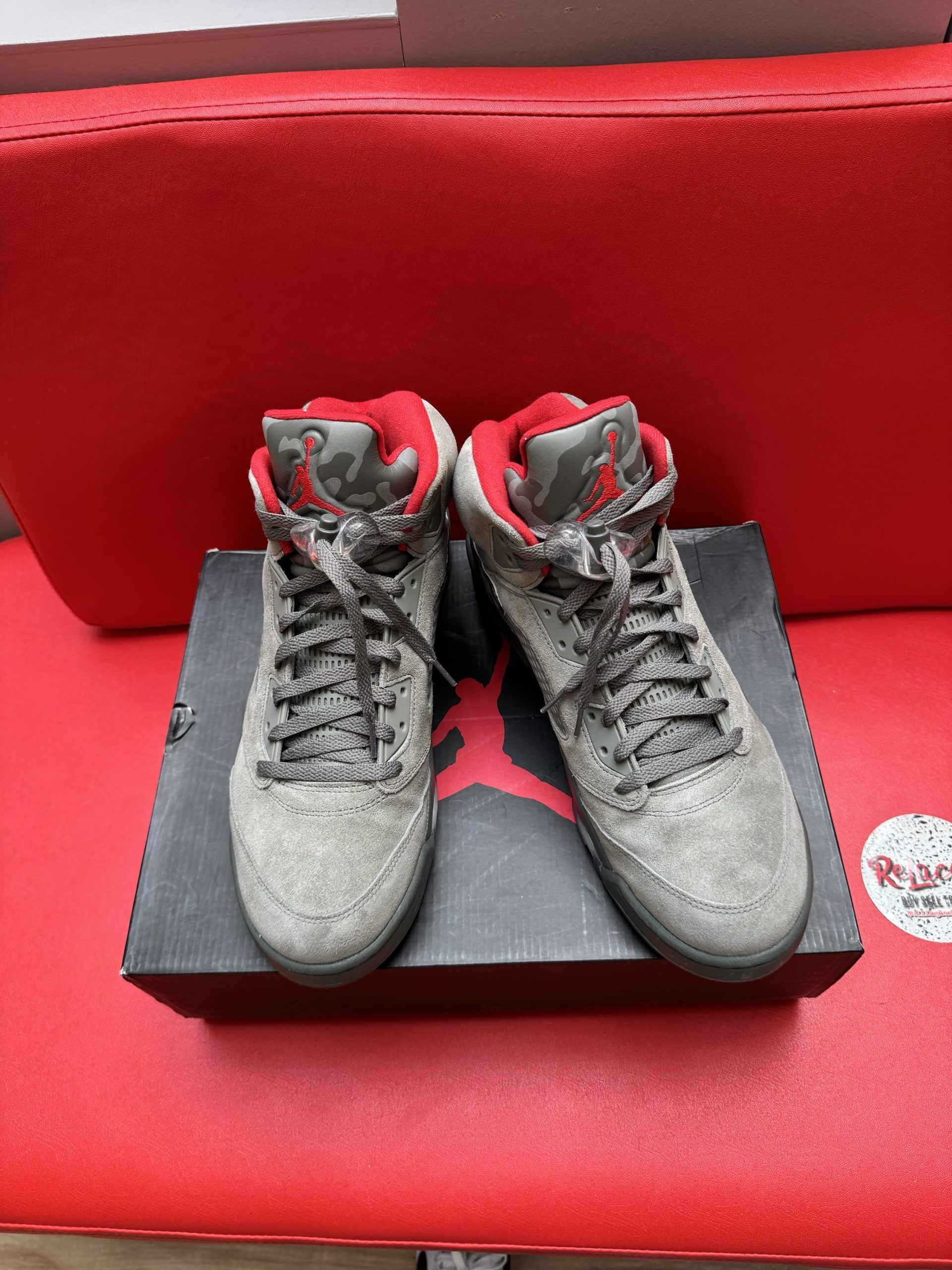 Gray and red Air Jordan 5 sneakers with a camouflage pattern, on a box, red background.