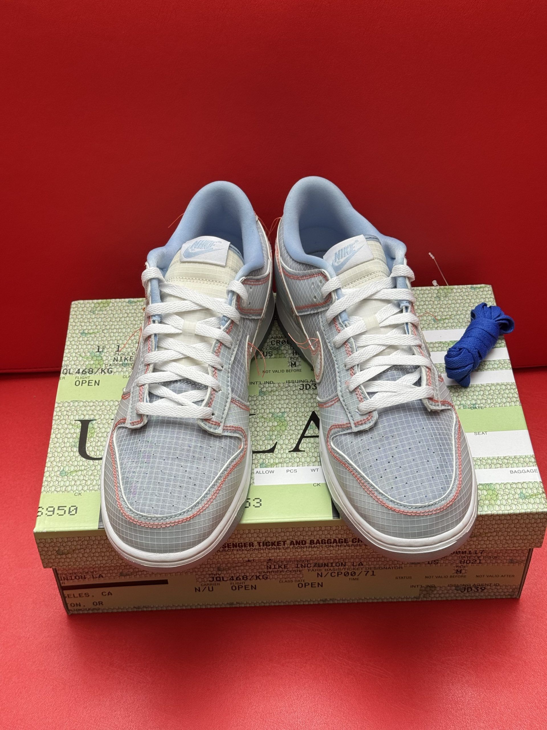 Light blue Nike Dunk Low sneakers with white laces, tan swoosh, on shoe box.