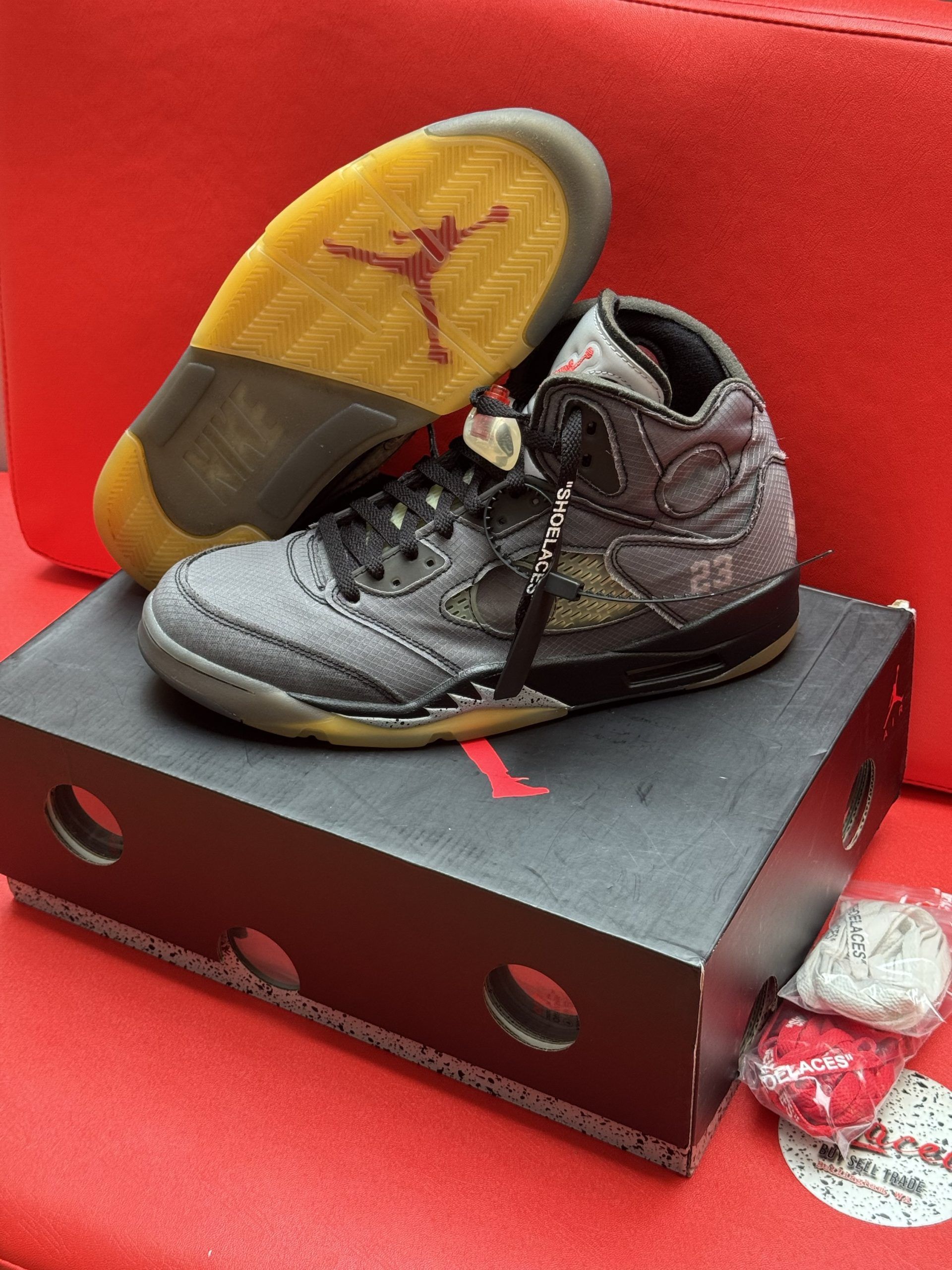 Air Jordan 5 Off-White sneakers on a black box, with a red sole and extra laces.