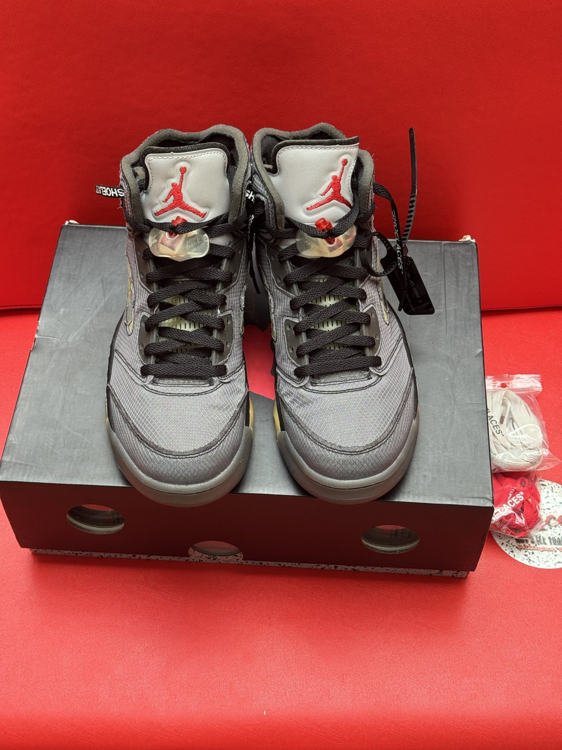 Air Jordan 5 Off-White sneakers on a black box, with a red sole and extra laces.