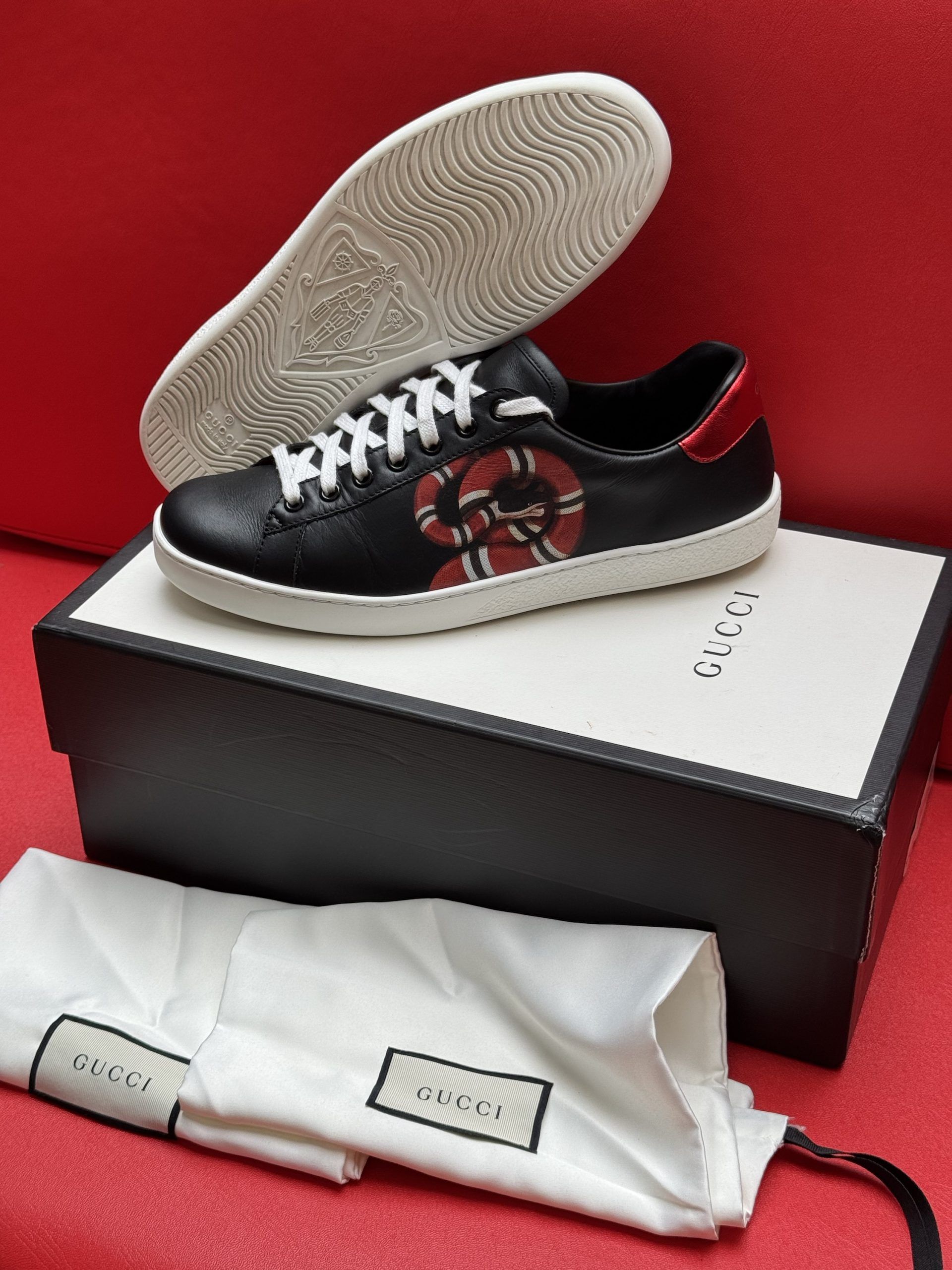 Black Gucci sneaker with snake design on a box, white sole, and bag.