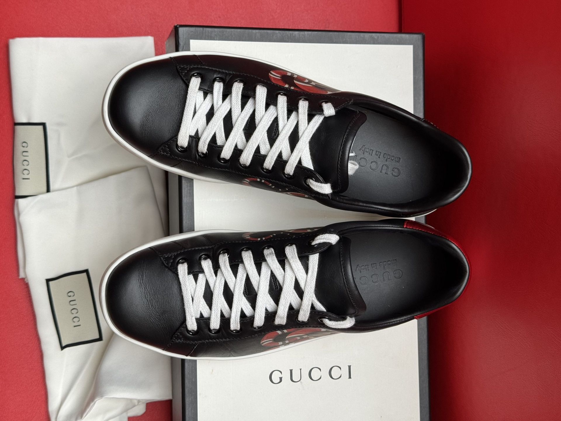 Black Gucci sneaker with snake design on a box, white sole, and bag.