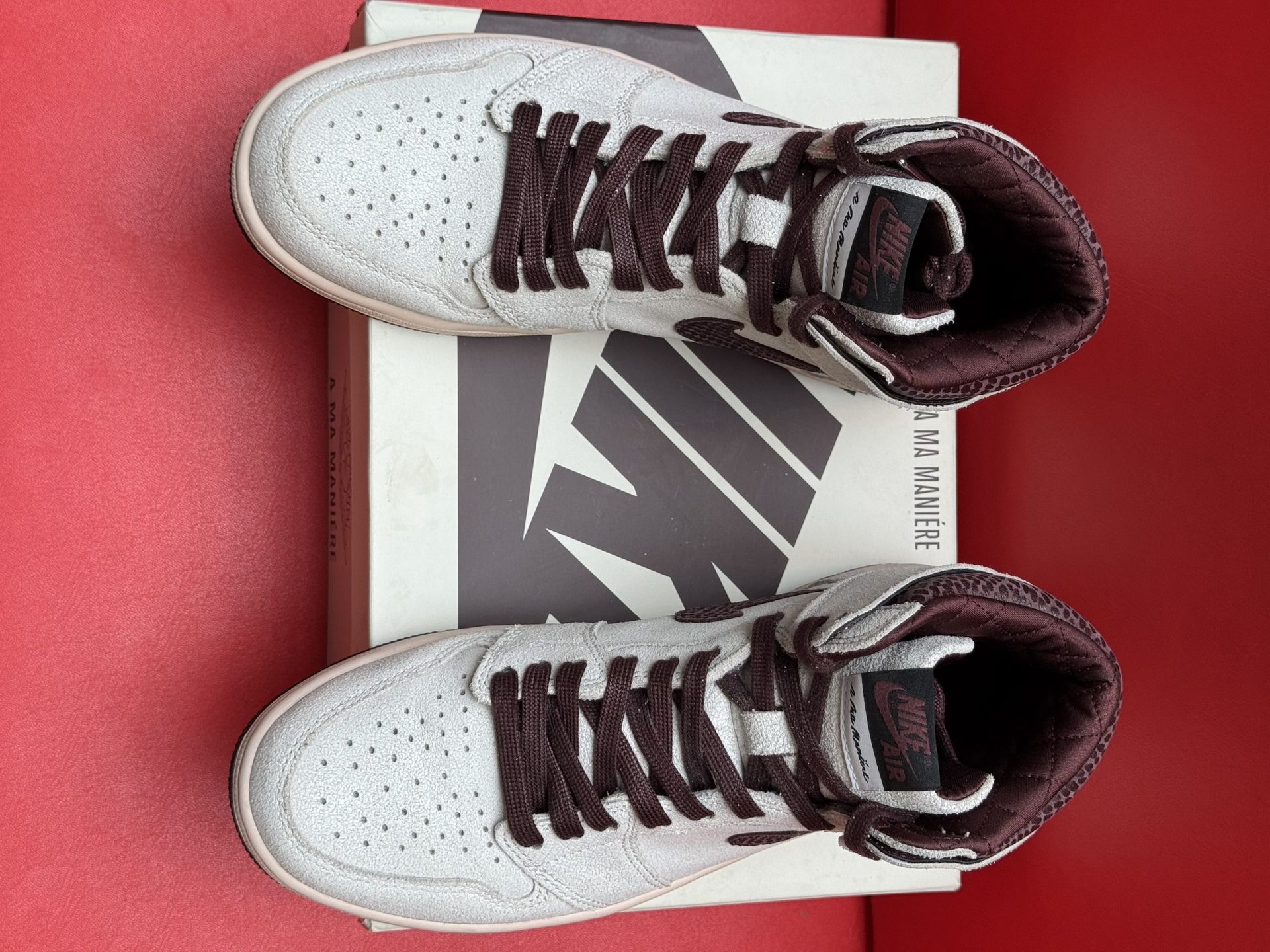 Air Jordan 1 high-top sneaker in white and dark red, on top of a box, with a red background.