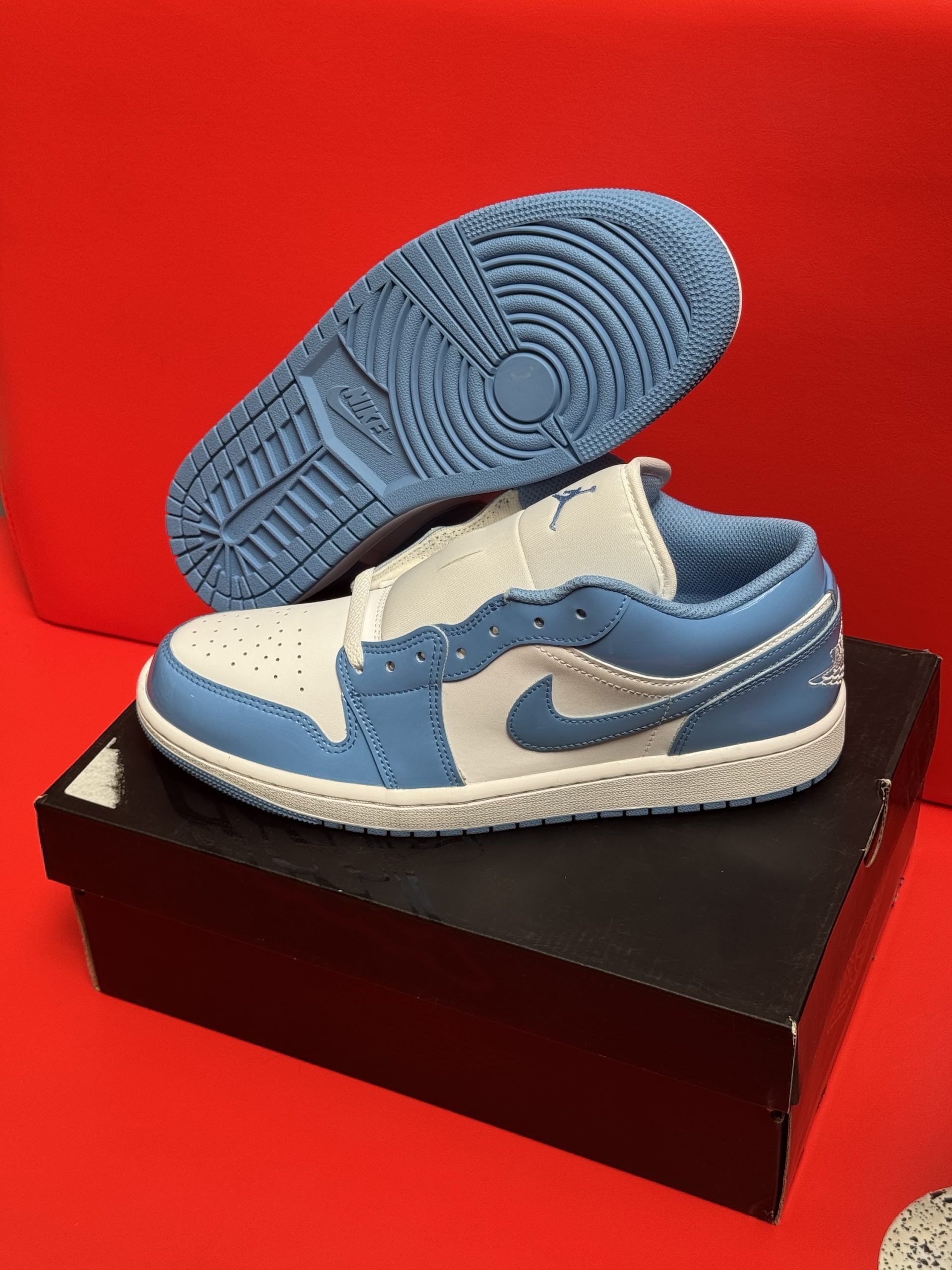 Baby blue and white Air Jordan 1 Low sneakers on a black box, with a red background.