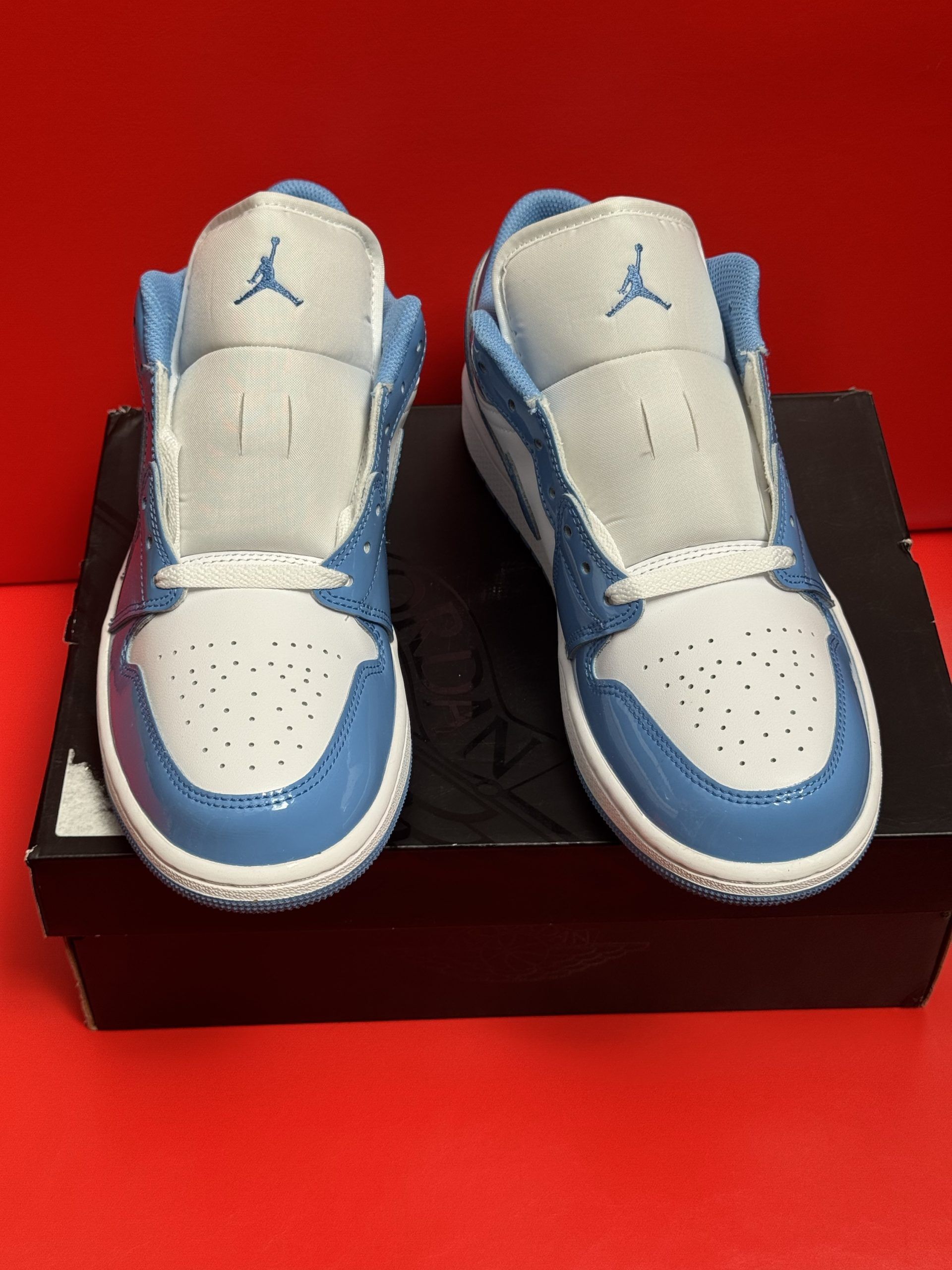 Baby blue and white Air Jordan 1 Low sneakers on a black box, with a red background.