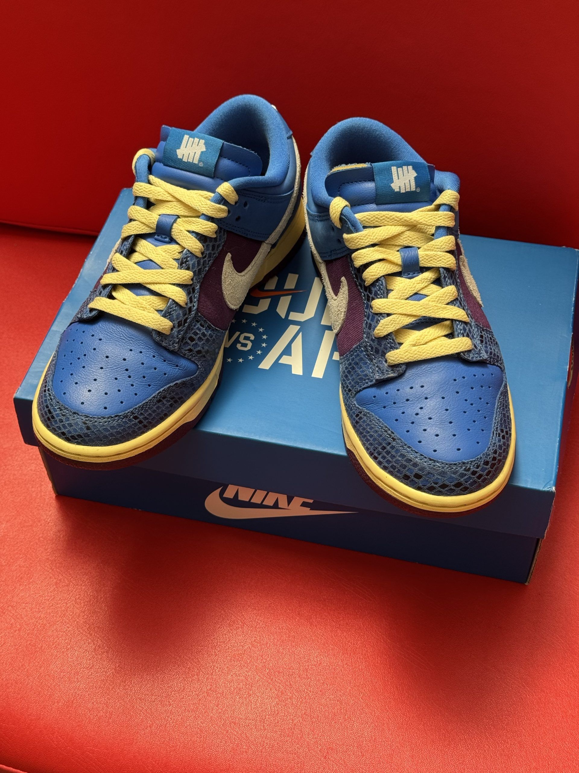 Blue and yellow Nike Dunk Low sneakers with white swoosh, on a blue box, sole visible.
