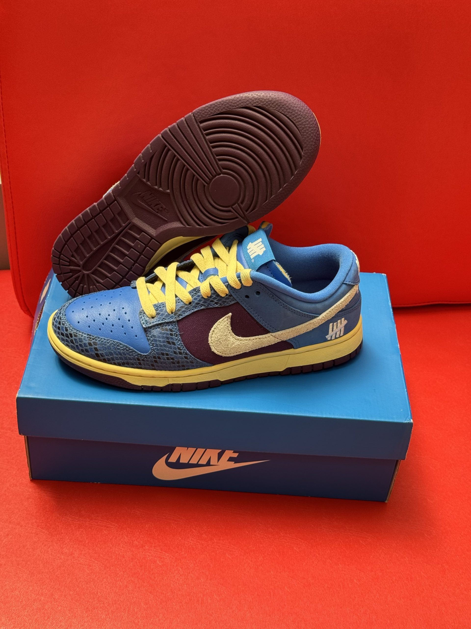 Blue and yellow Nike Dunk Low sneakers with white swoosh, on a blue box, sole visible.