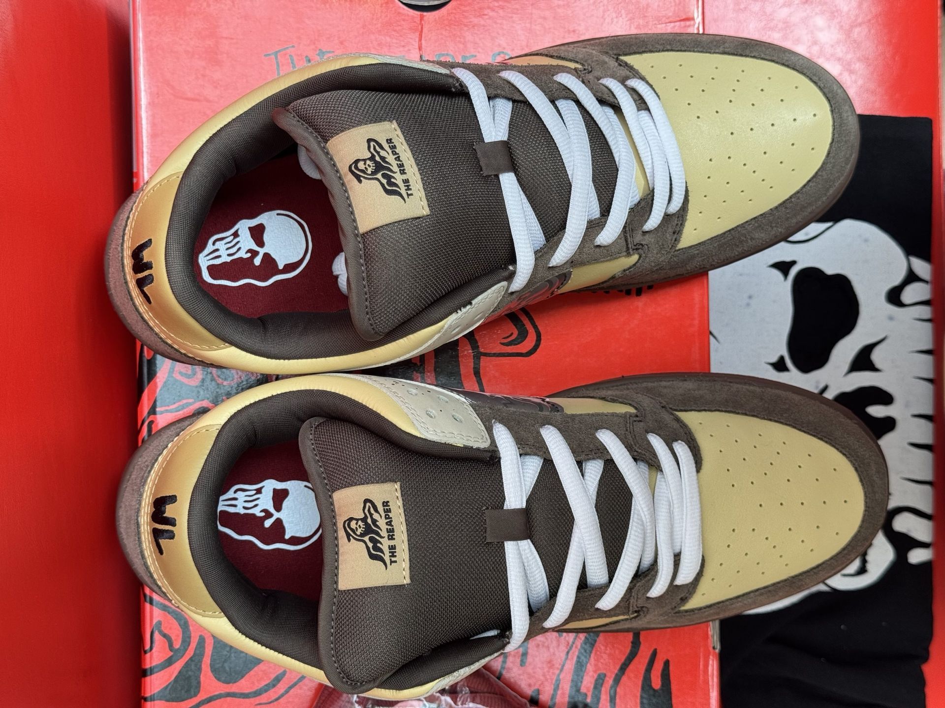 Pair of brown and tan sneakers with red accents on a red box, near a skull-themed bag.