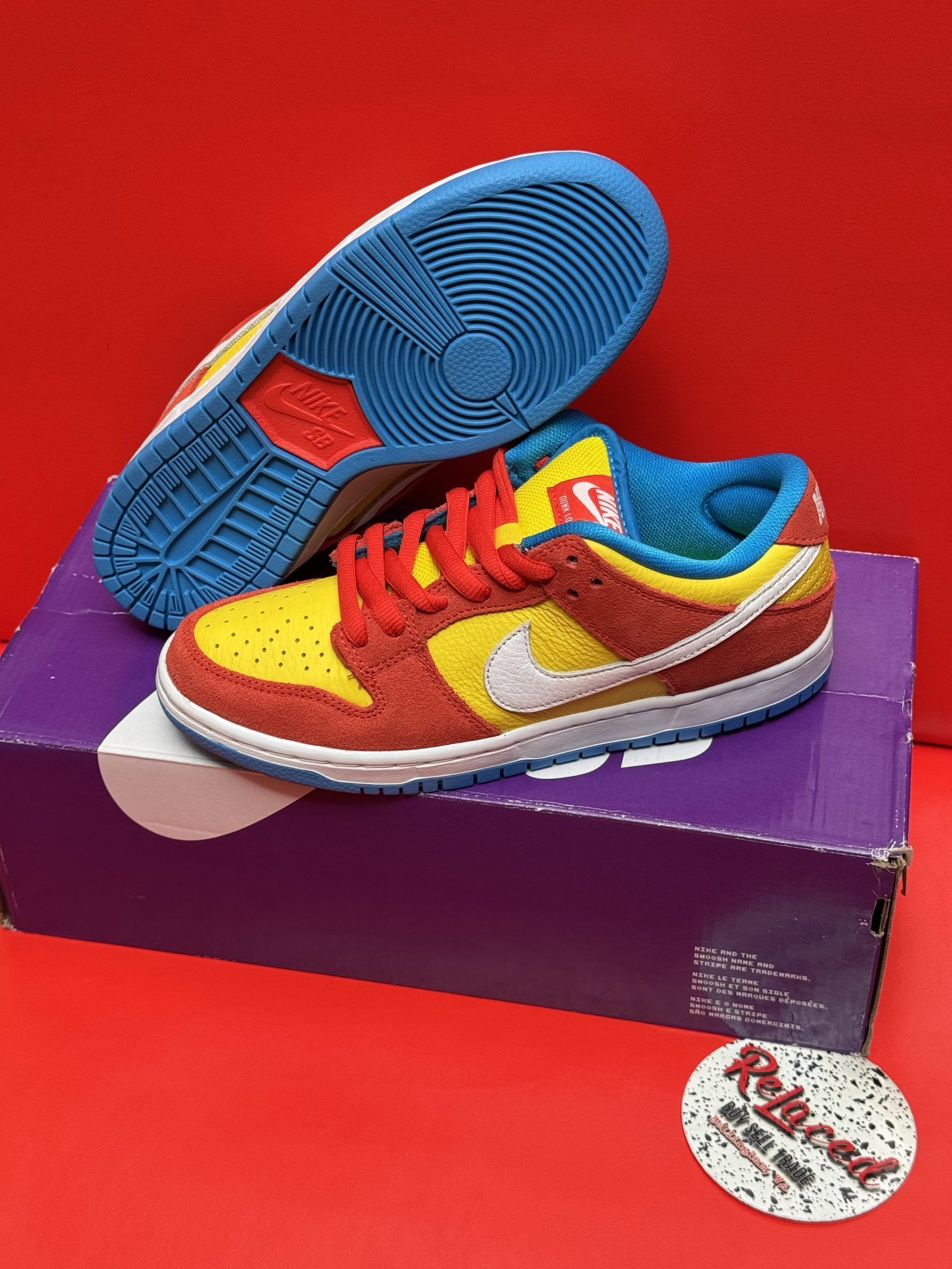 Nike Dunk low sneakers, red and yellow, white swoosh, on purple box, blue soles.