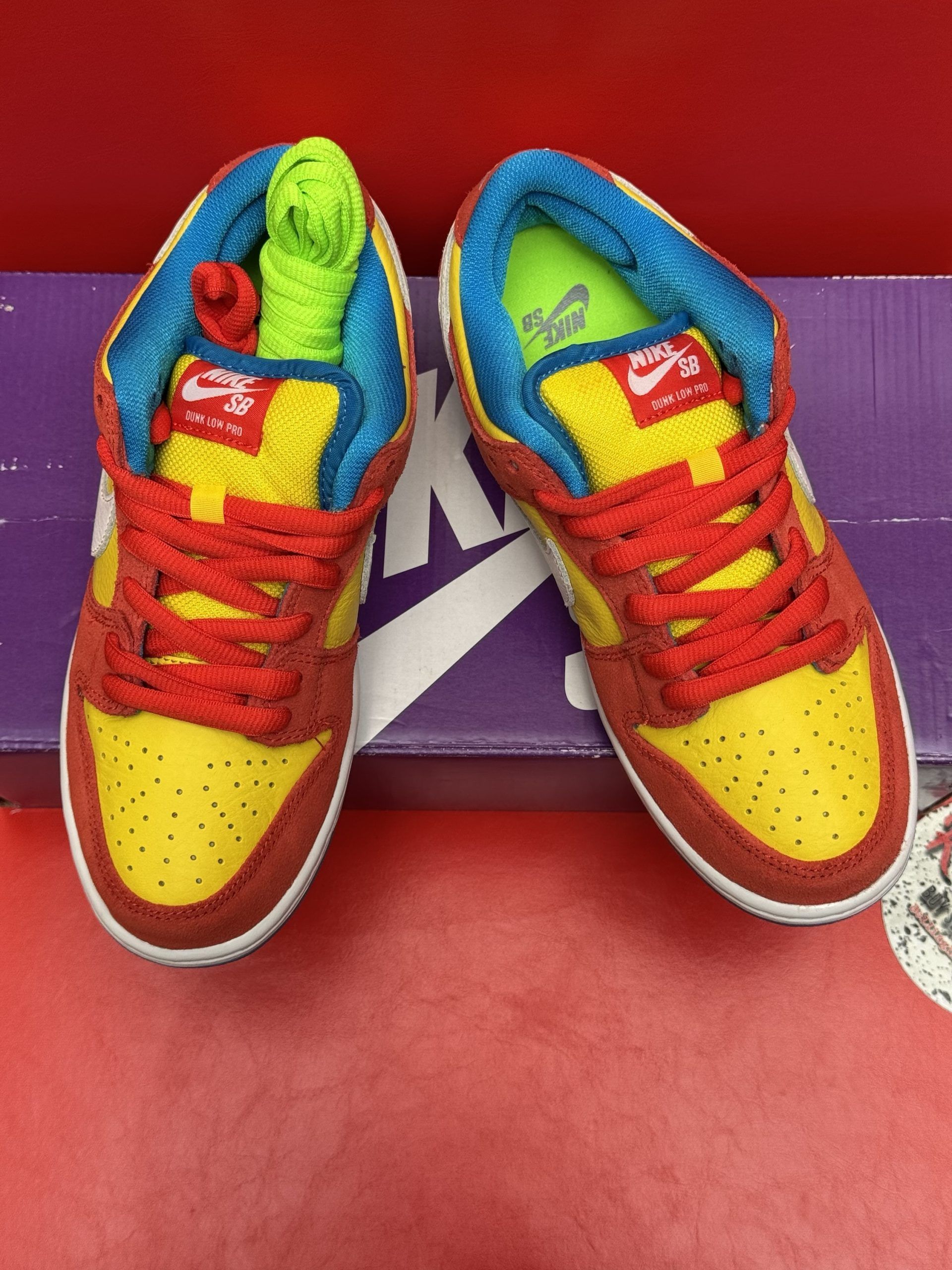 Nike Dunk low sneakers, red and yellow, white swoosh, on purple box, blue soles.