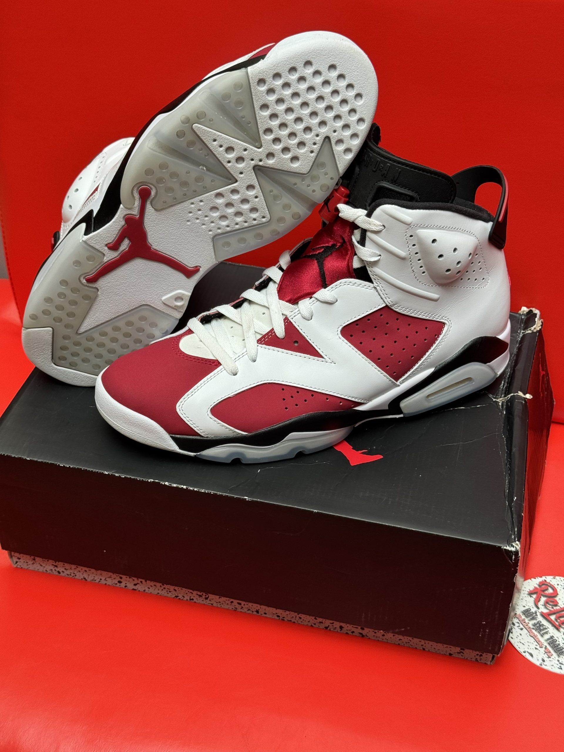 Air Jordan 6 Retro sneakers, white and red, on a black shoebox with a red background.