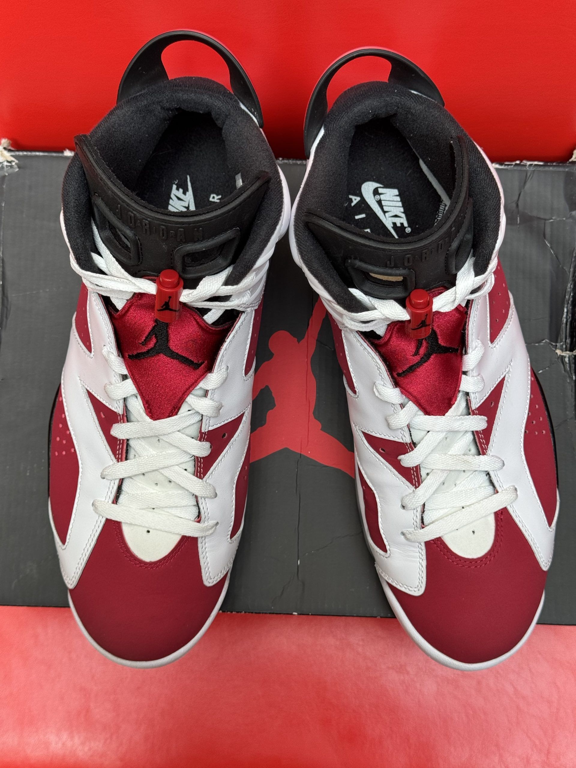 Air Jordan 6 Retro sneakers, white and red, on a black shoebox with a red background.