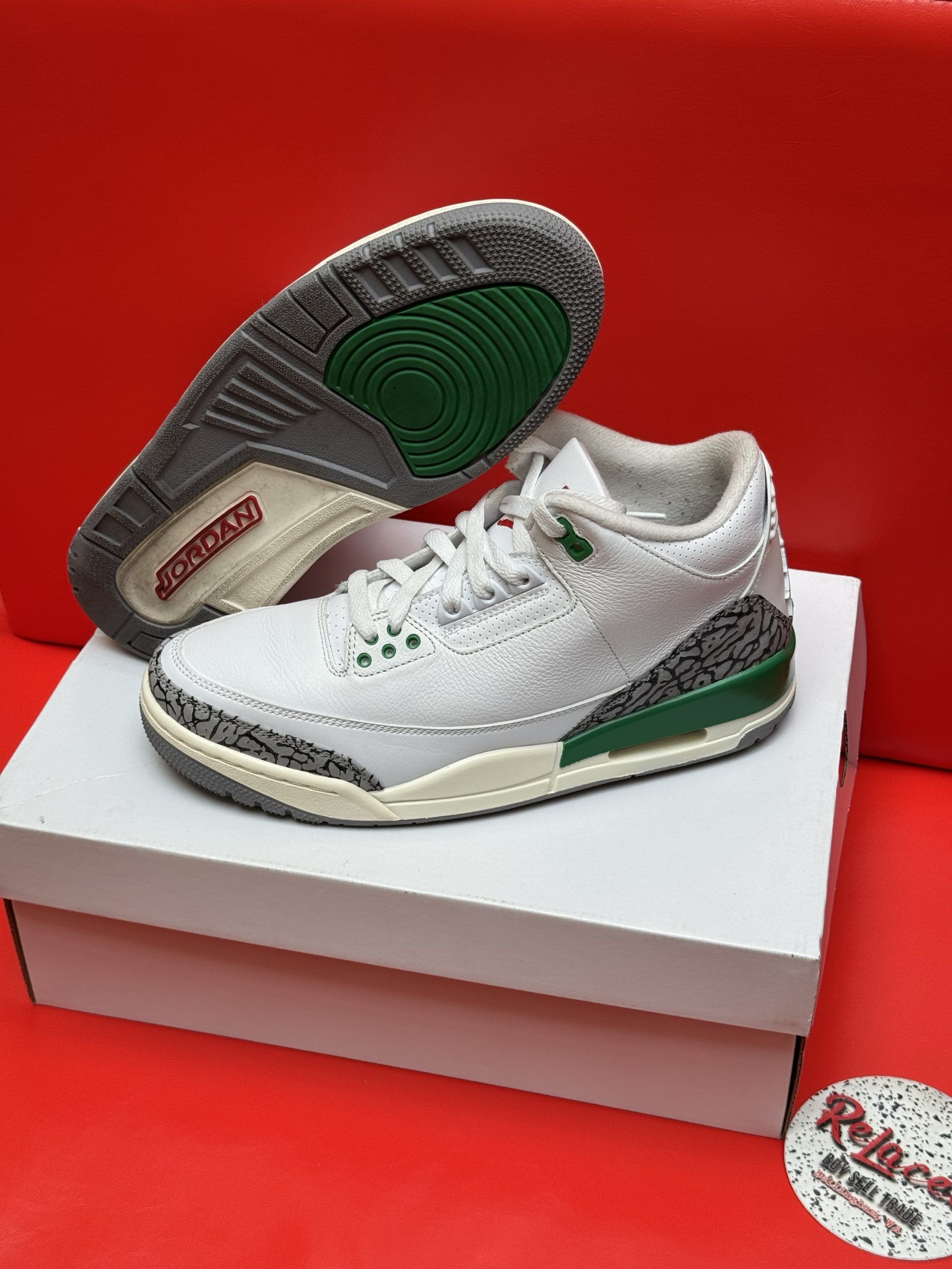 White, green, and gray Air Jordan 3 sneakers on a white box, red background.