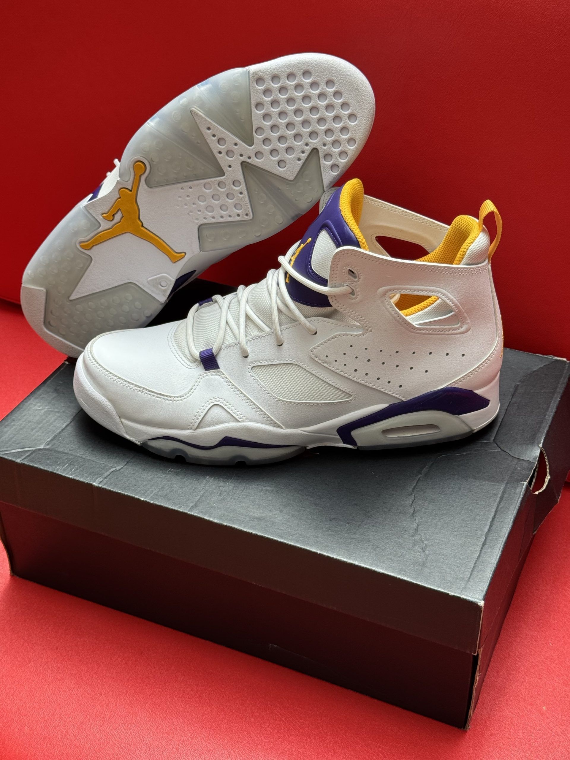 White and purple Air Jordan sneakers with yellow accents, atop a shoebox, on a red surface.