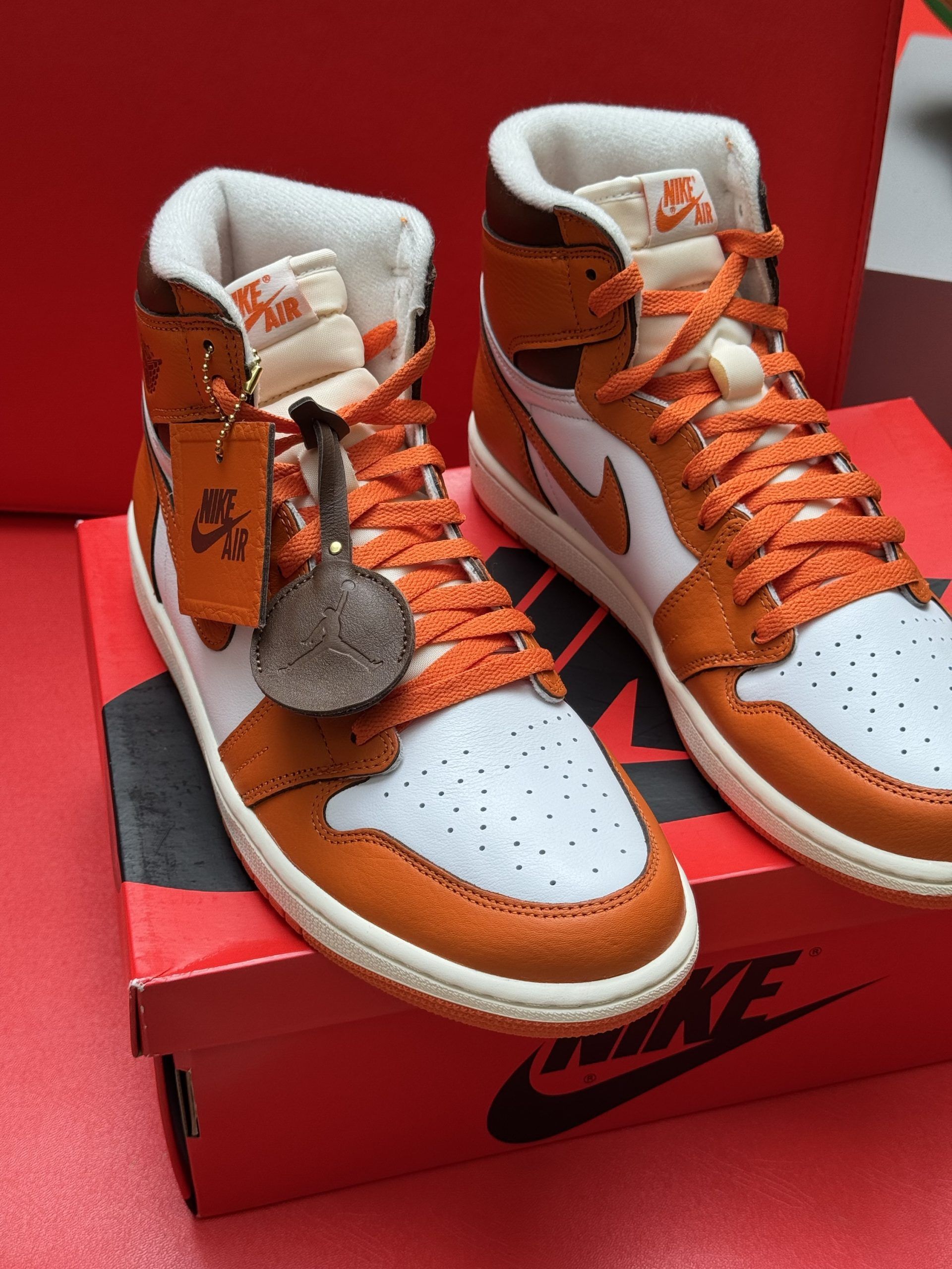Orange and white Air Jordan 1 sneaker, box, and shoe sole on a red surface.