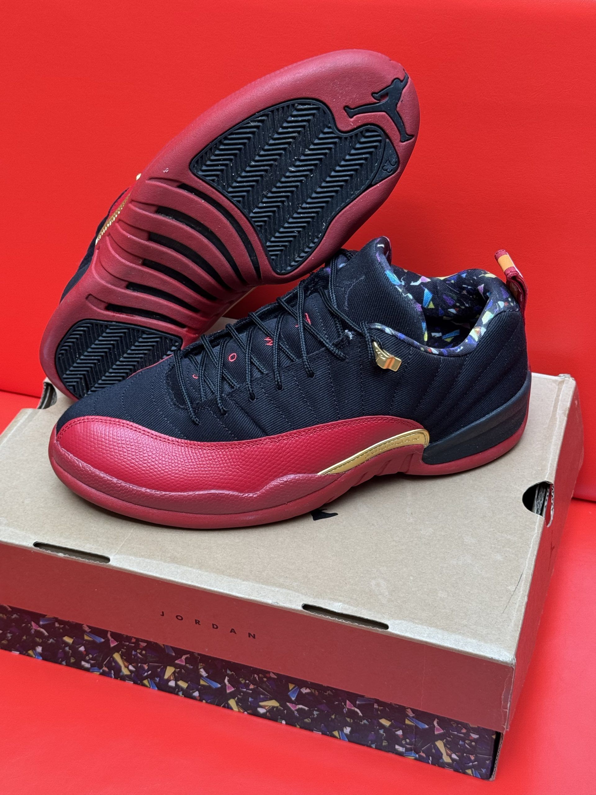 Black and red Jordan 12 sneakers on a box, sole up.