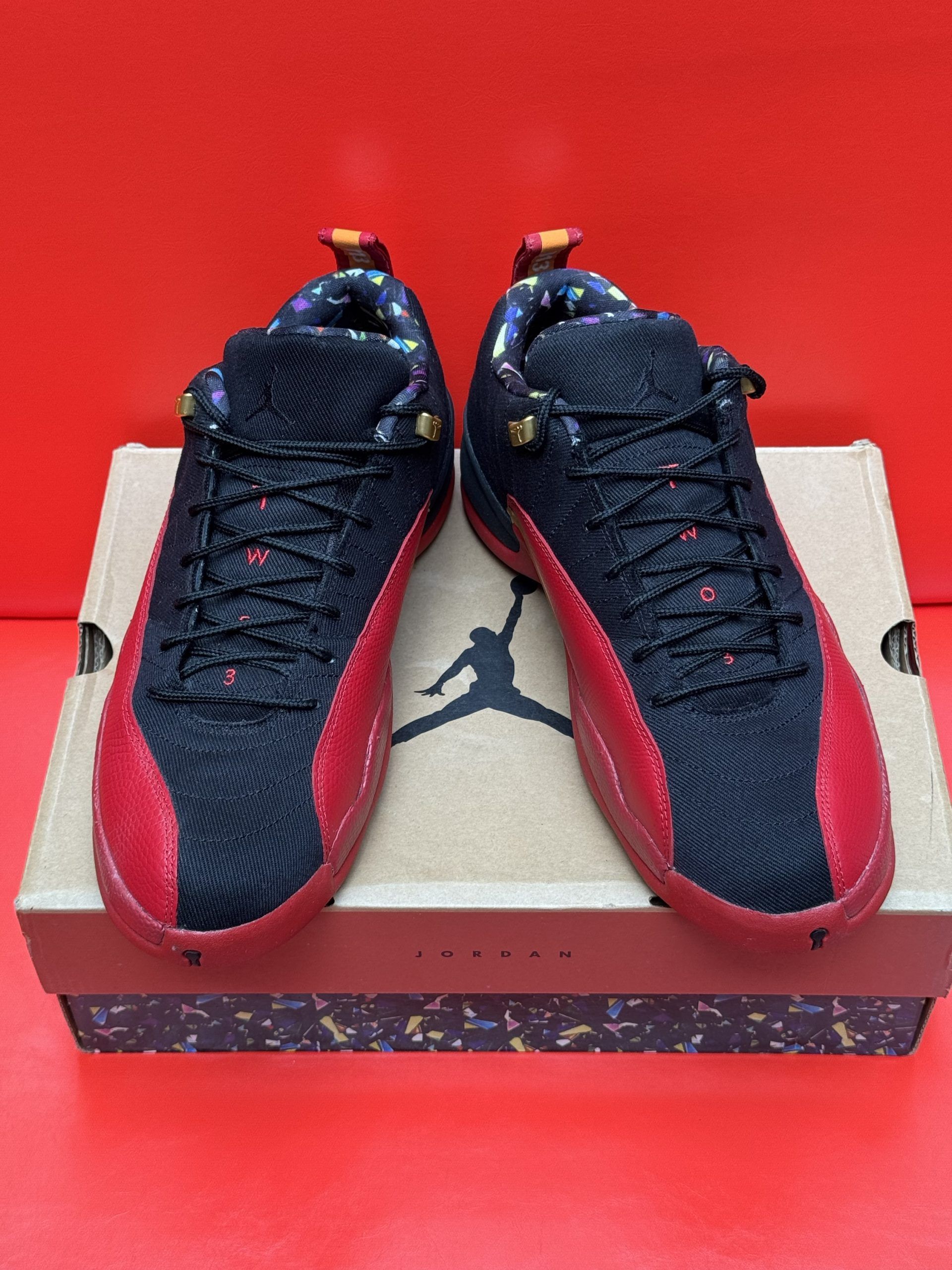 Black and red Jordan 12 sneakers on a box, sole up.