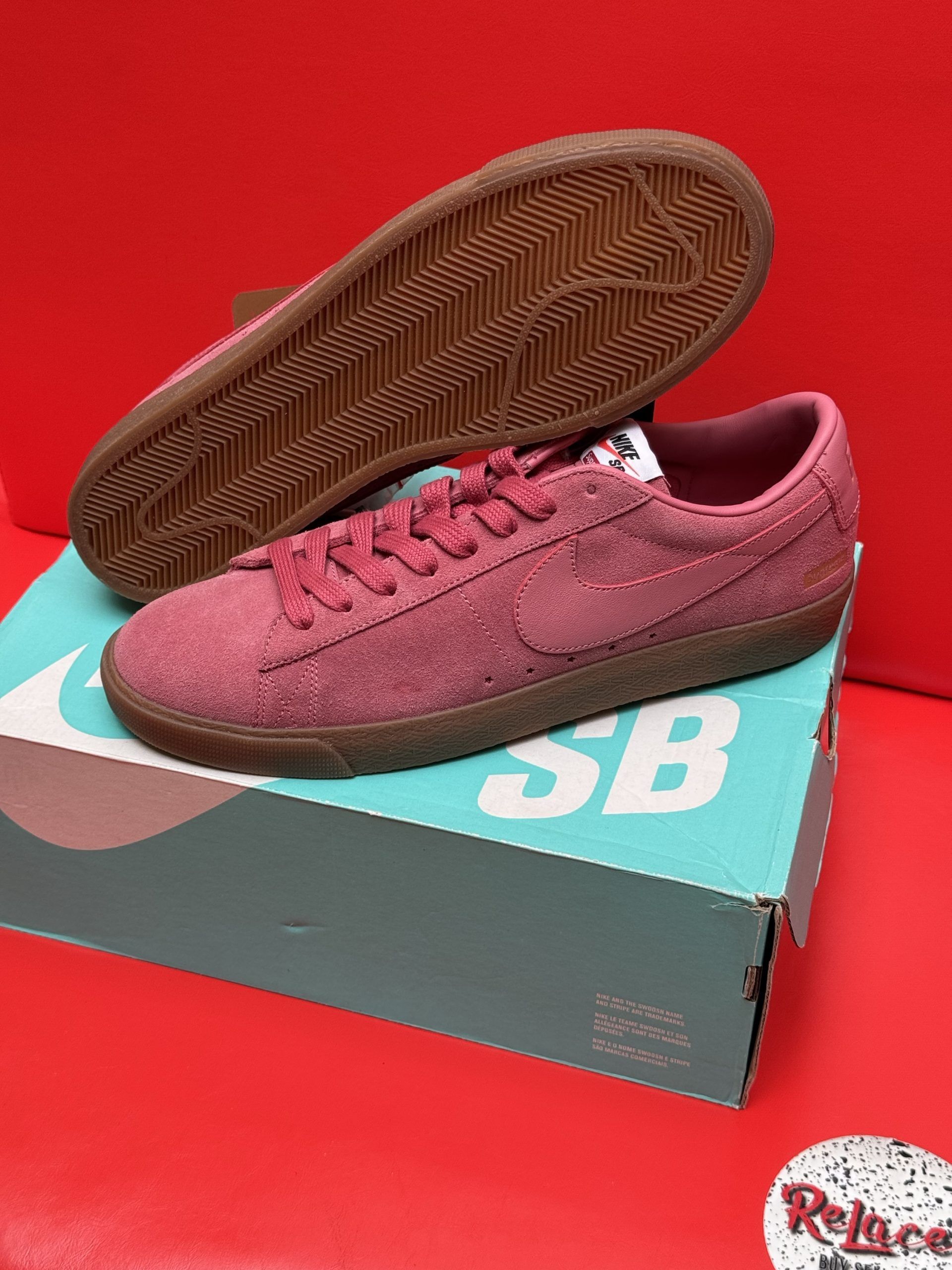 Pink Nike SB Blazer shoes with brown soles on a teal box against a red background.