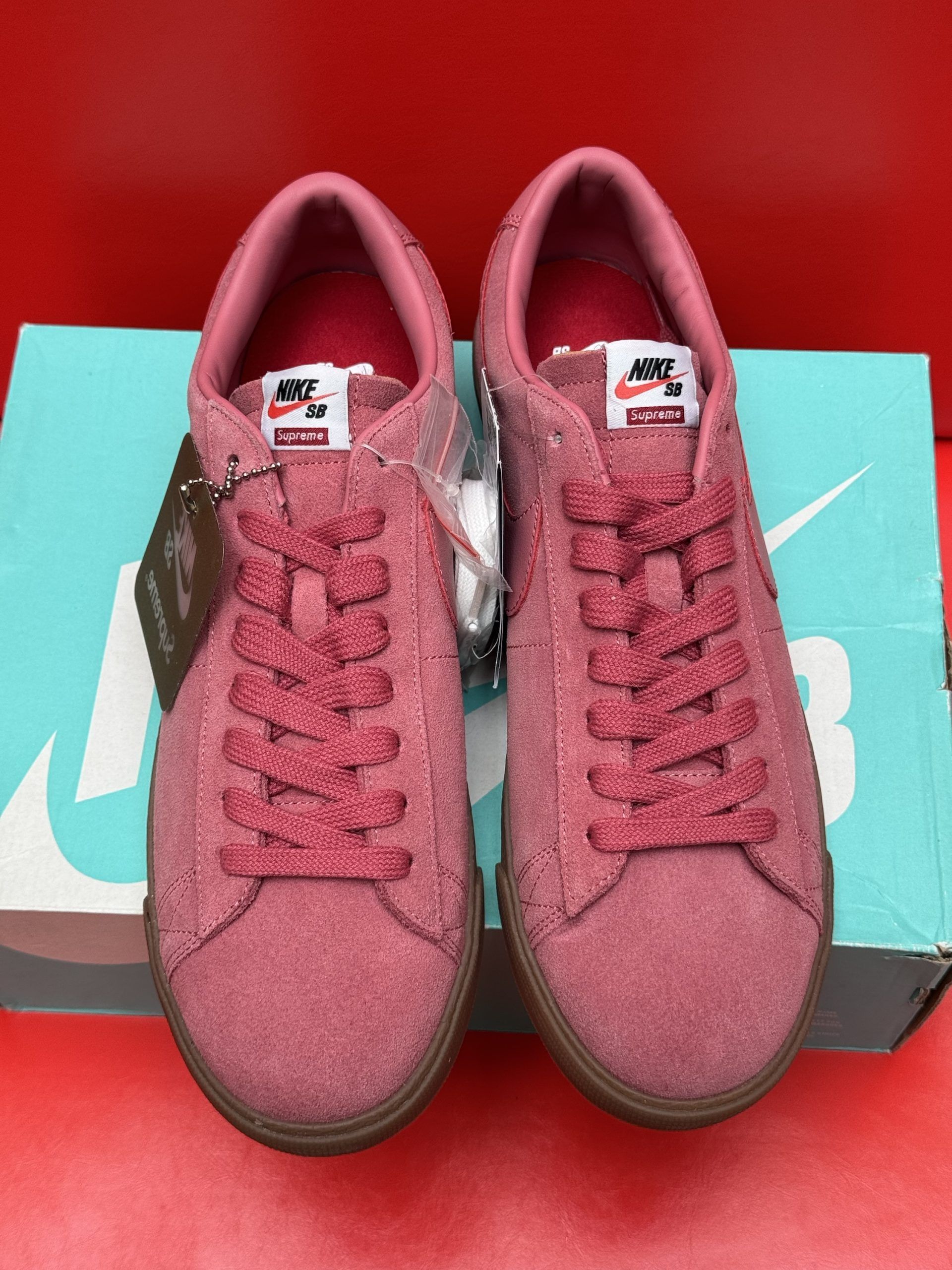 Pink Nike SB Blazer shoes with brown soles on a teal box against a red background.