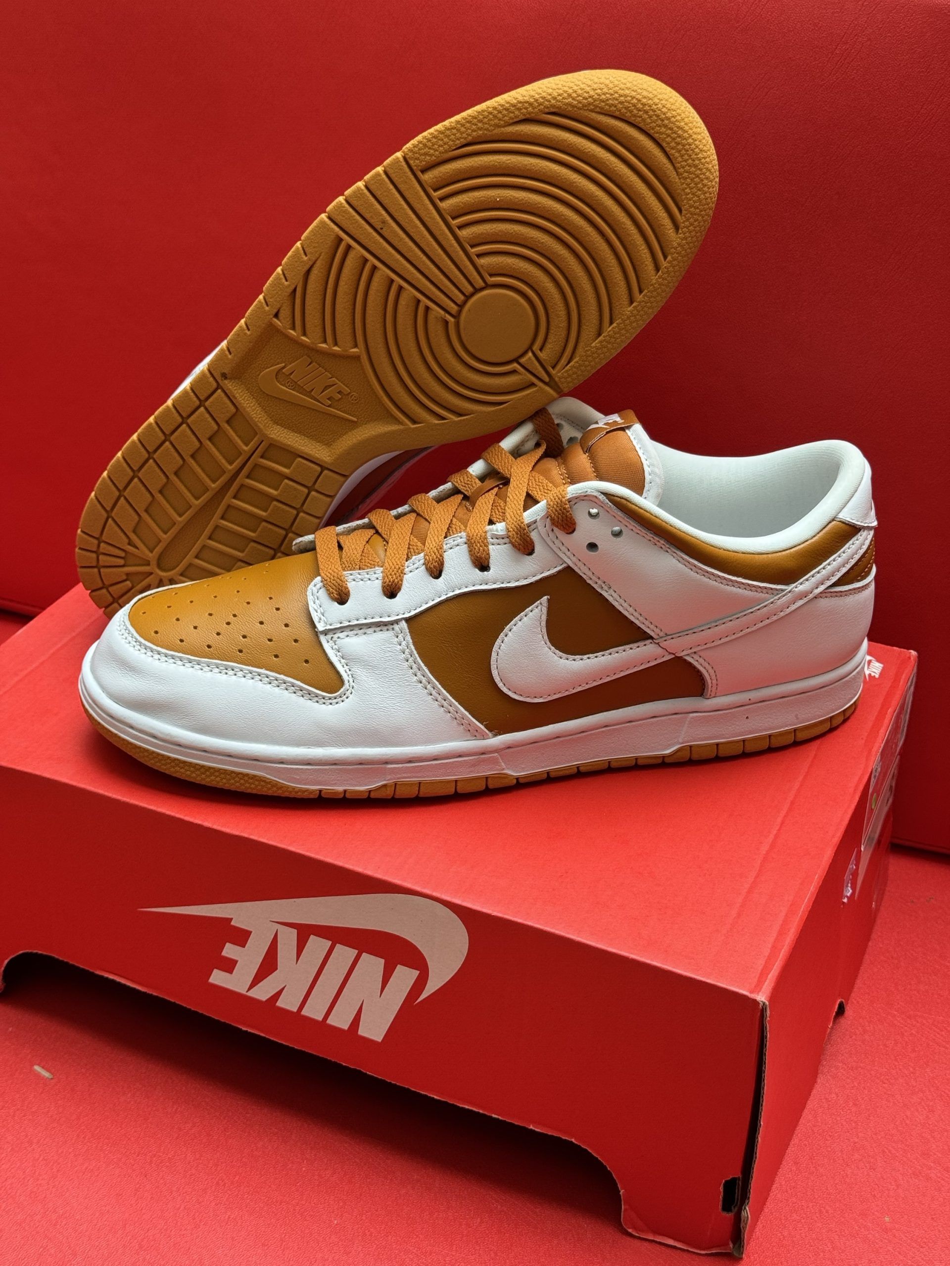 Nike Dunk Low sneakers, white and brown leather, on a red shoebox, brown sole against a red background.