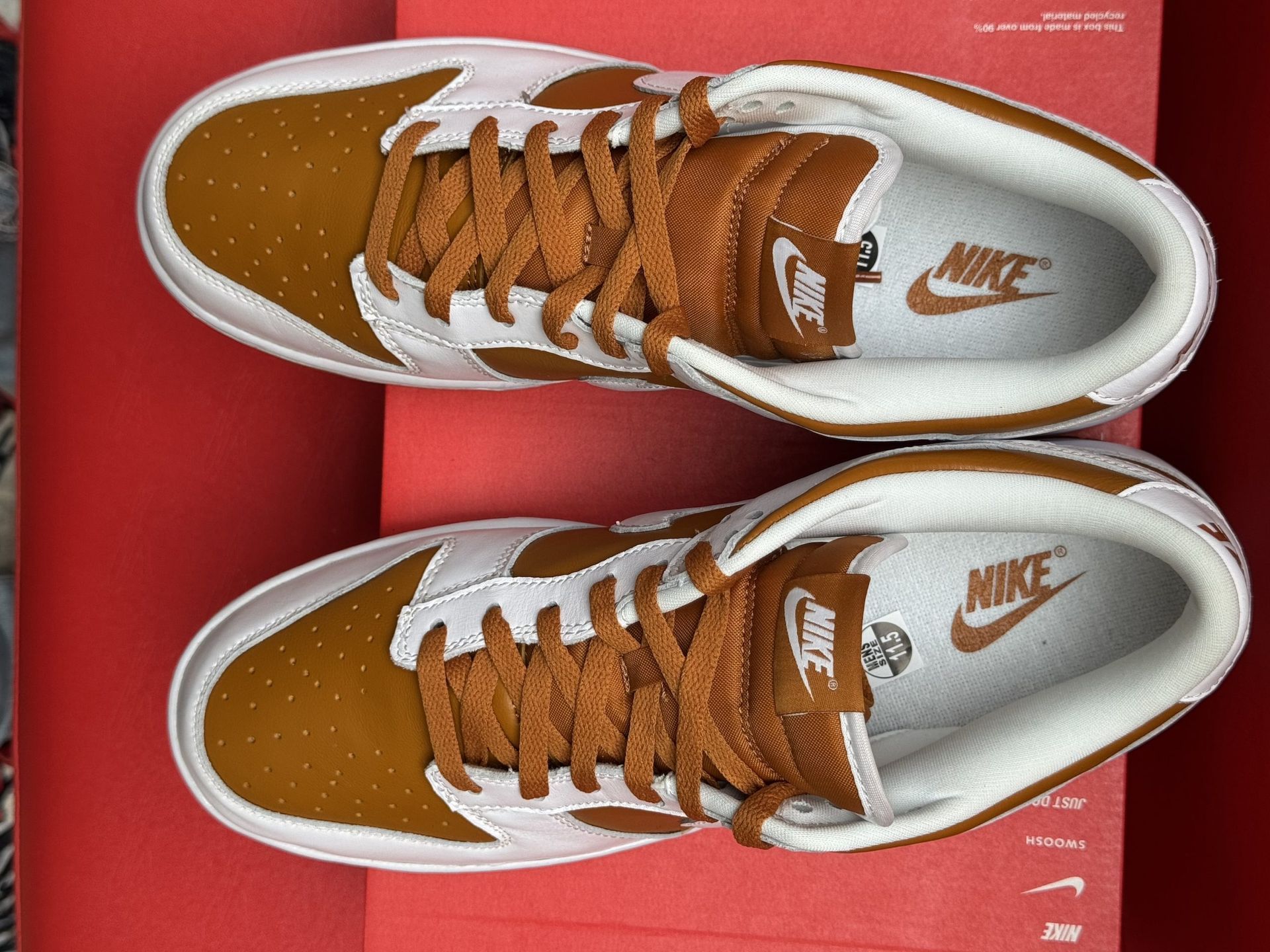 Nike Dunk Low sneakers, white and brown leather, on a red shoebox, brown sole against a red background.