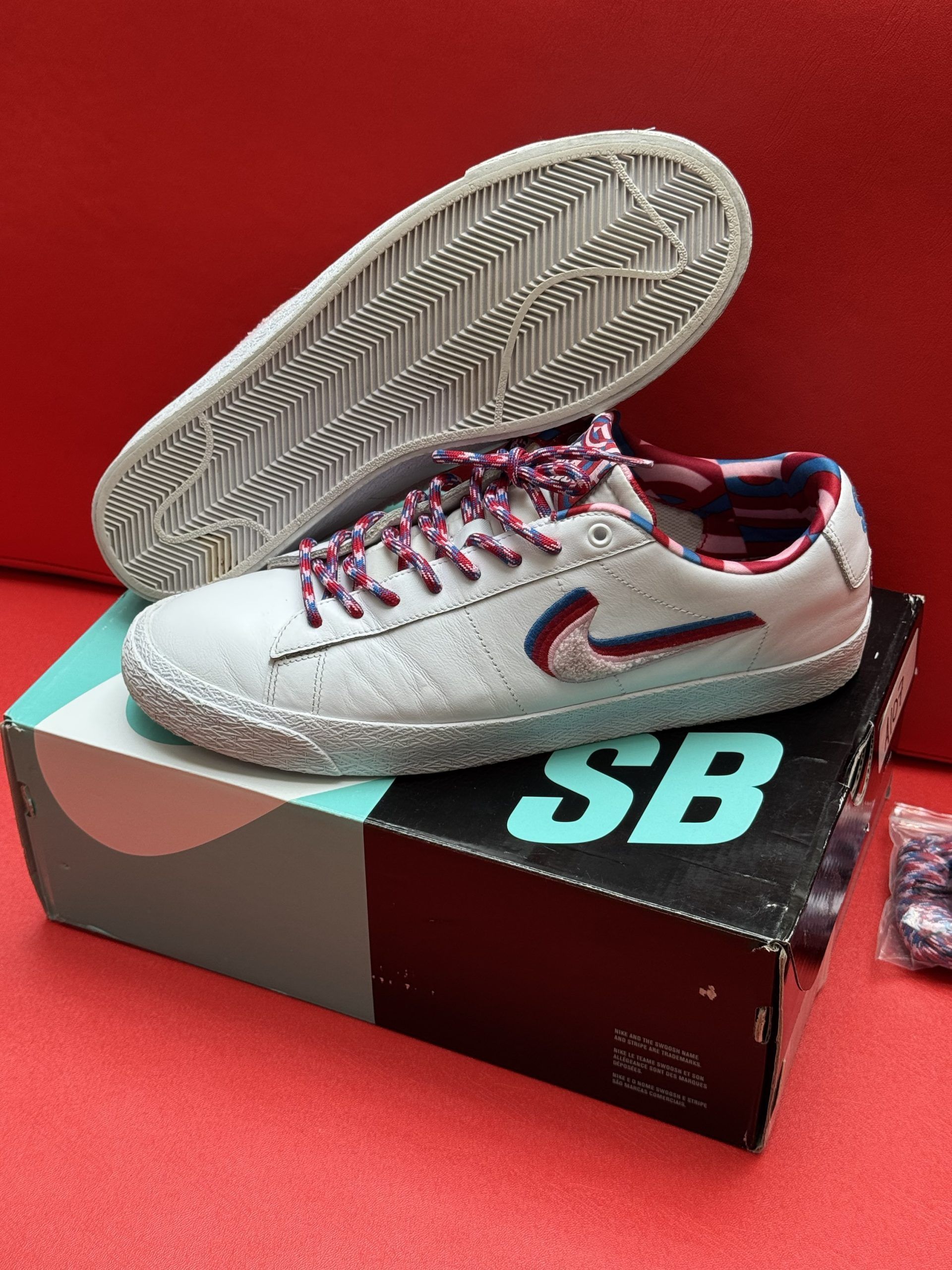 White Nike SB Blazer low top sneaker with red and blue accents, laces, and box.