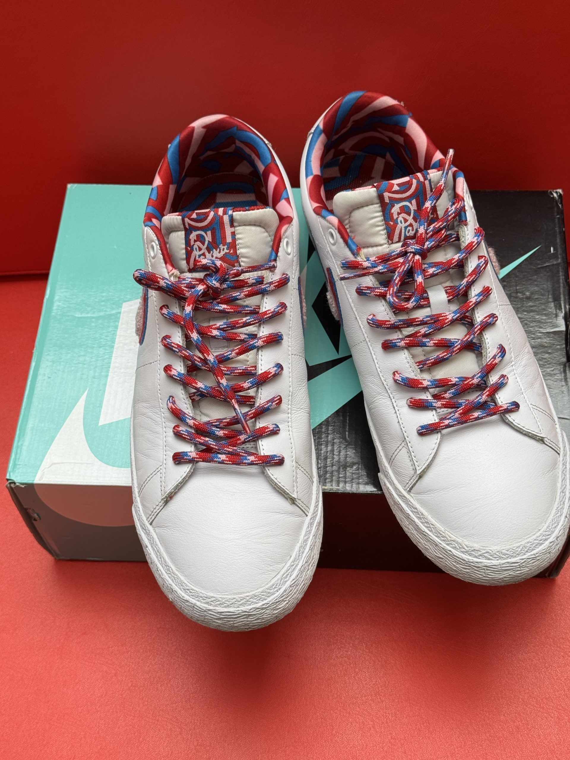 White Nike SB Blazer low top sneaker with red and blue accents, laces, and box.