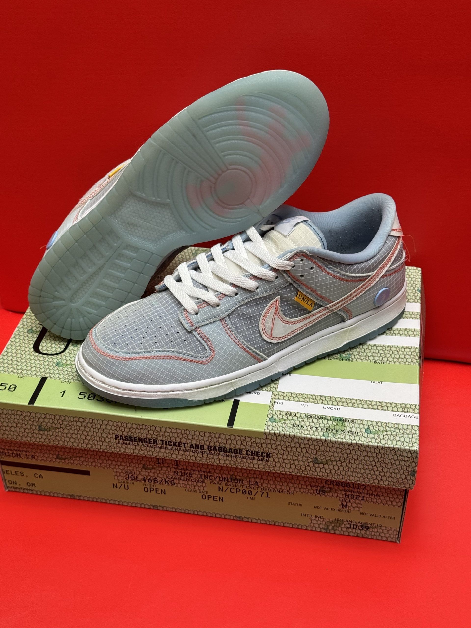 Blue and beige Nike Dunk Low sneakers with white laces on a box, red background.