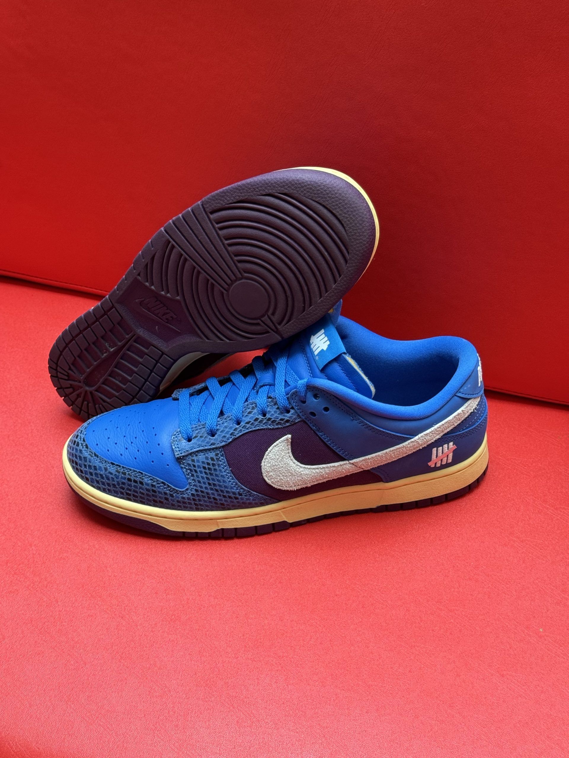 Blue Nike Dunk Low sneakers with purple and white accents on a red surface.