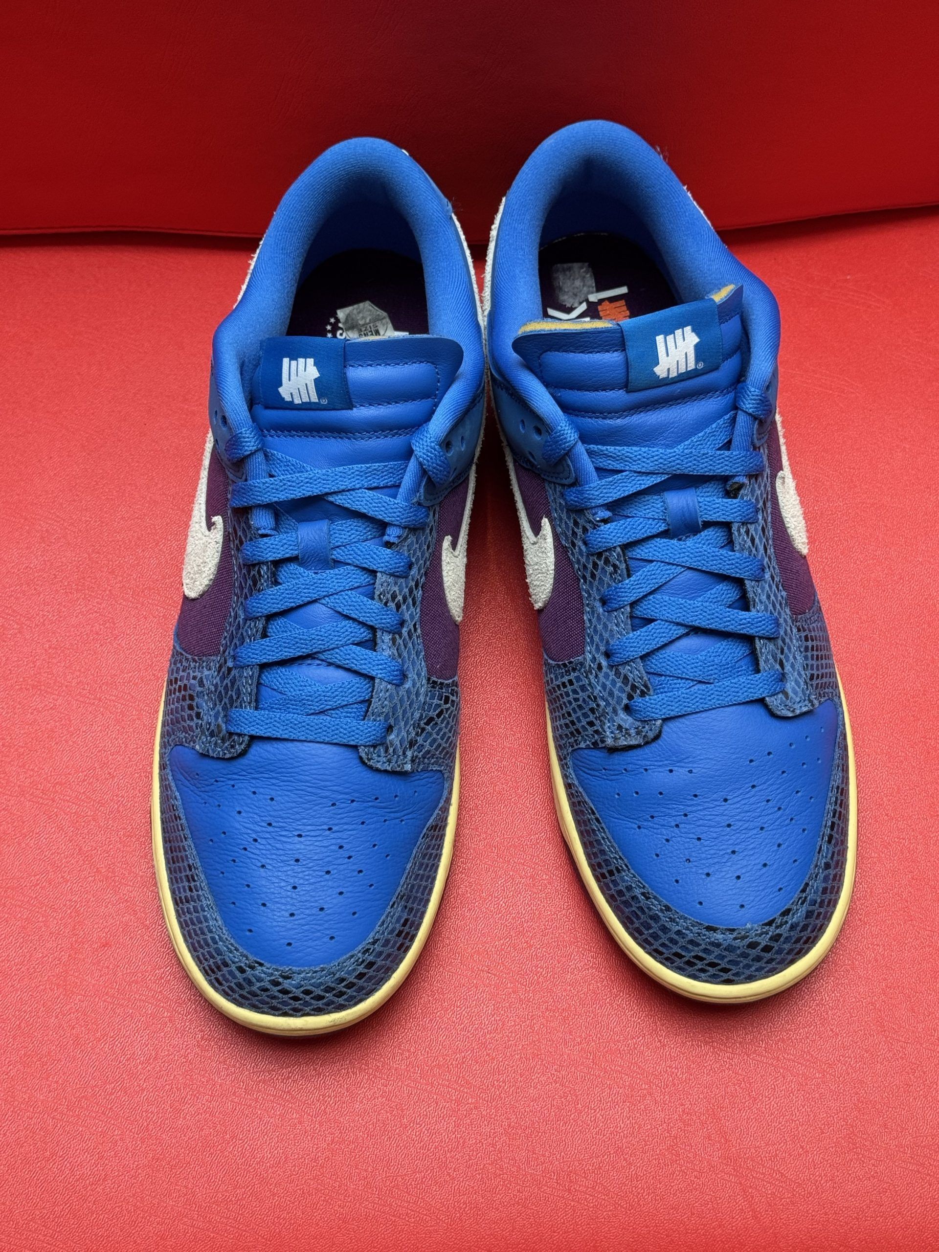 Blue Nike Dunk Low sneakers with purple and white accents on a red surface.