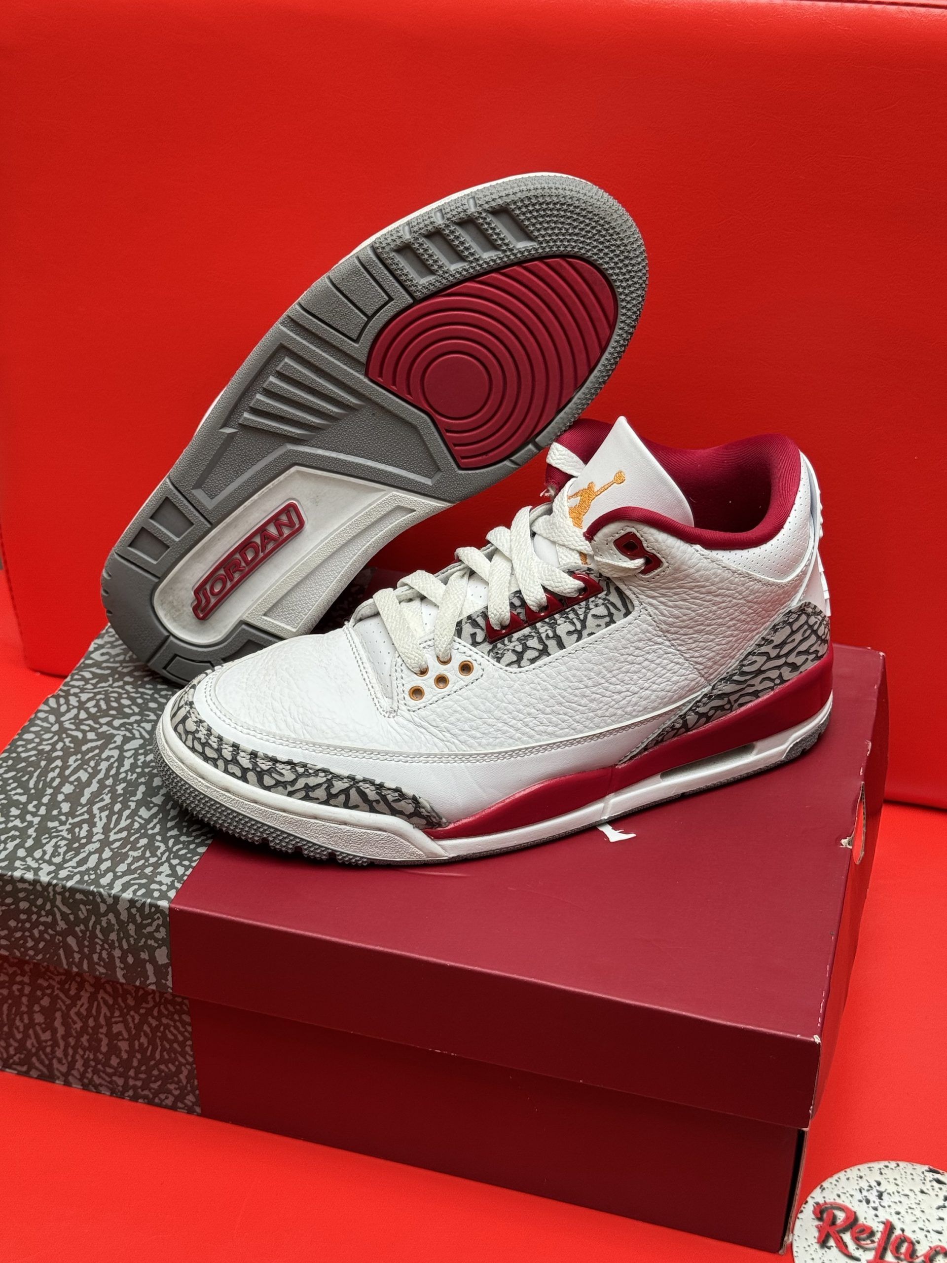 Air Jordan 3 sneakers in white, red, and grey, on a red shoebox, set against a red background.
